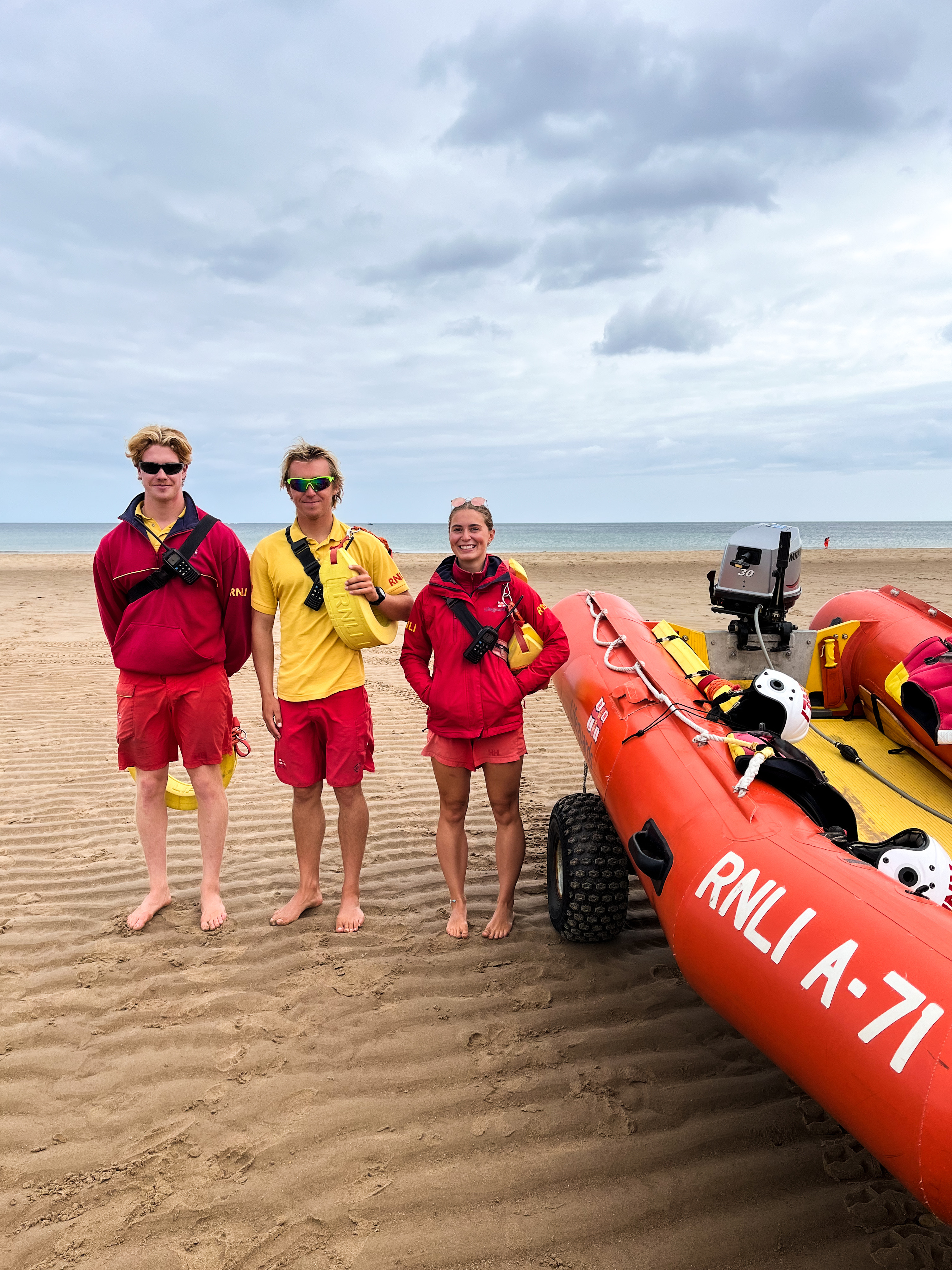 Three lifeguards aligned standing to the left of a Inshore Lifeboat on the beach