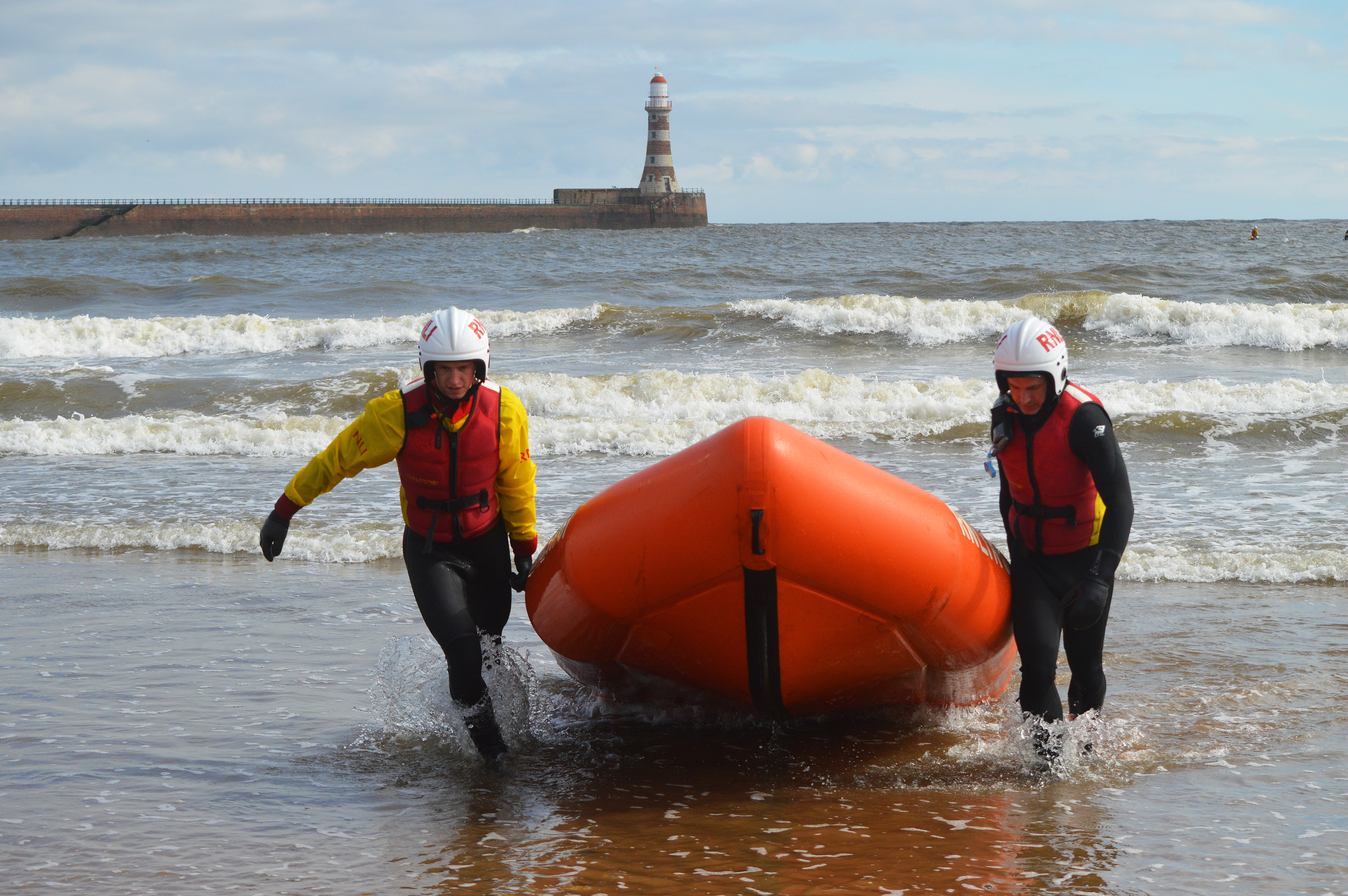 Two lifeguards in training dragging an inshore lifeboat out the water. 