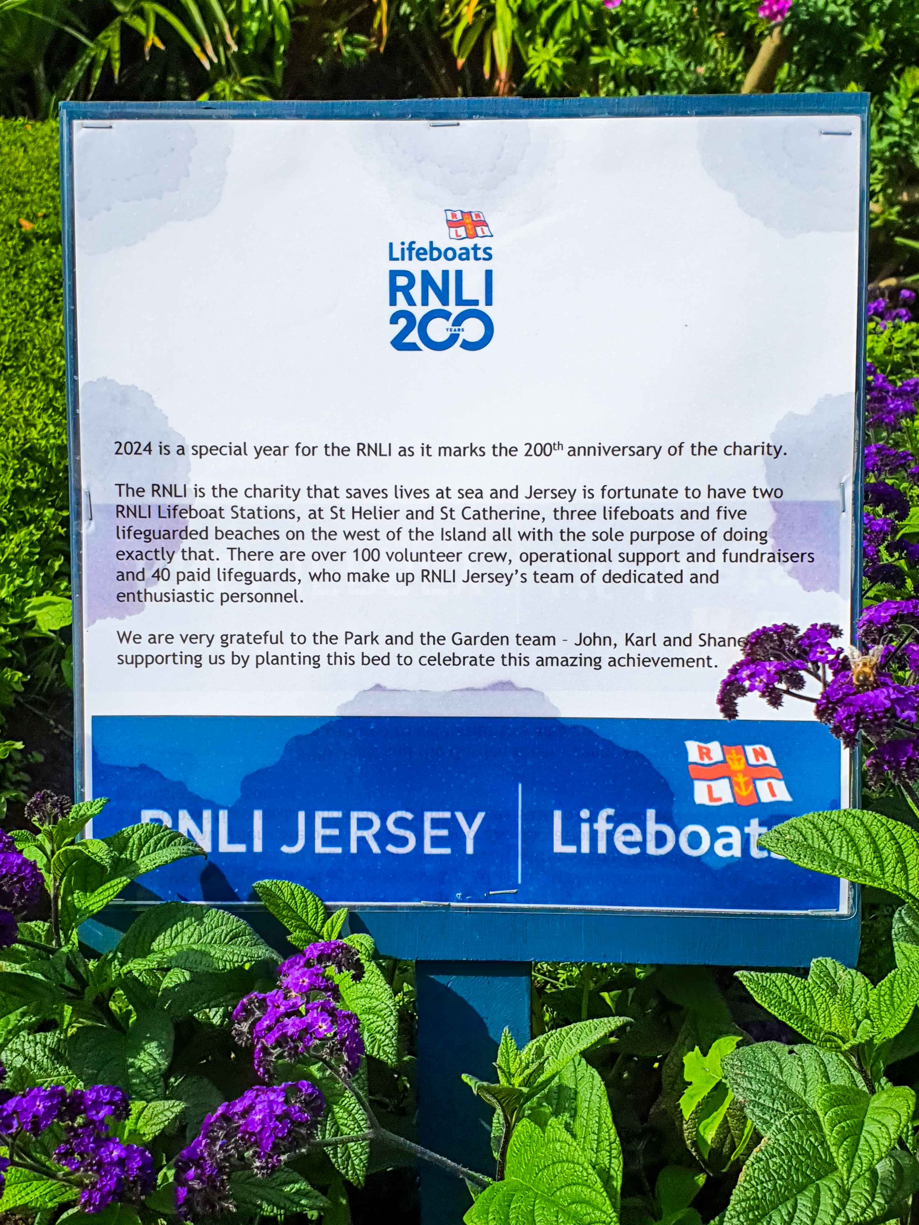 The sign beside the flowerbed dedicates the flowerbed to the RNLI, giving a brief history and ending with the words "We are very grateful to the Park and the Garden team - John, Karl and Shane - for supporting us by planting this bed to celebrate this amazing achievement."