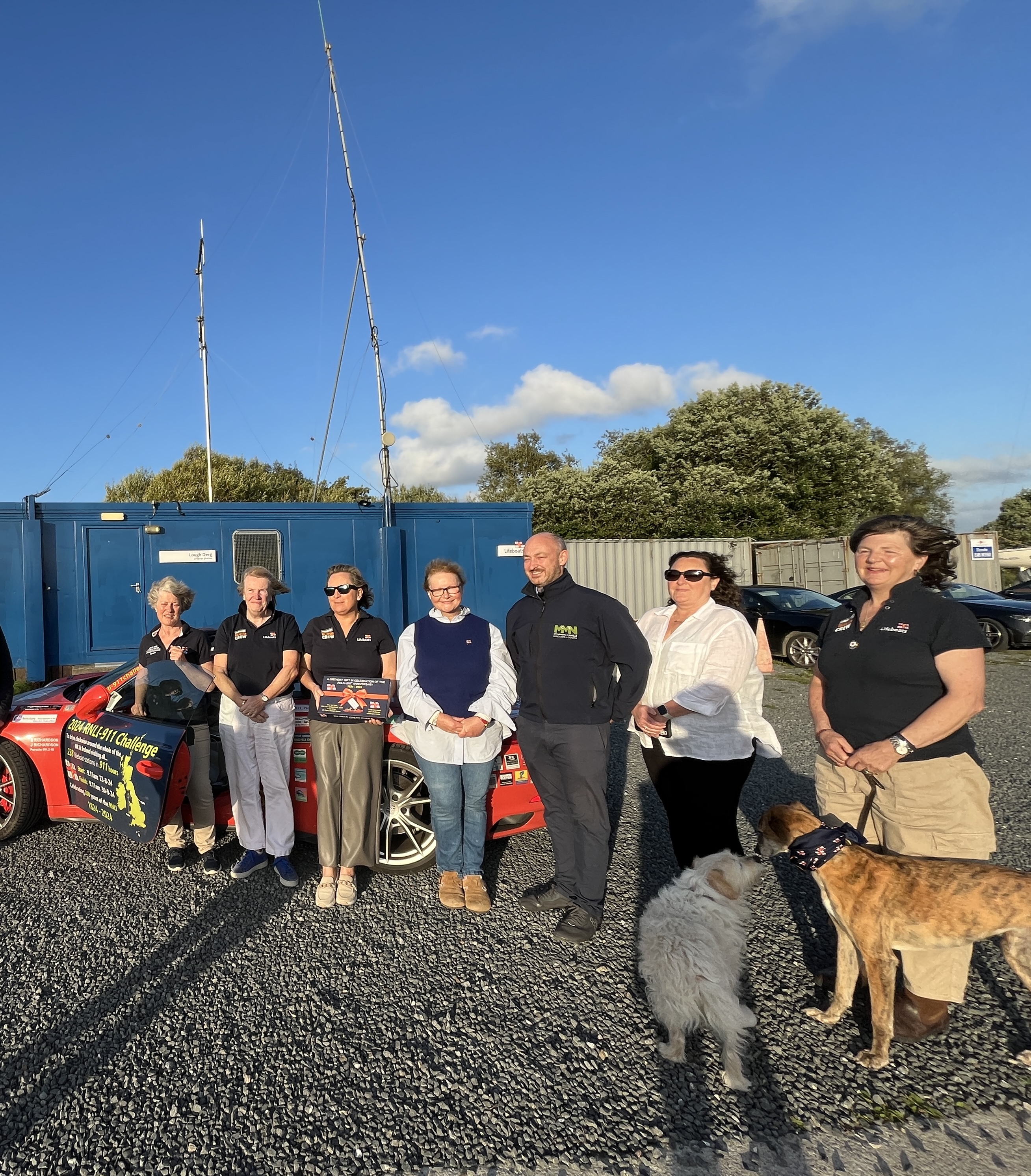 Lough Derg RNLI volunteers being presented with a gift from Michael and Vanessa Nagle, sponsors of this visit of Porsche 911 challenge, in honour of their father - all stand in front of the Porsche, 2 of the volunteers dogs are in the photographs also