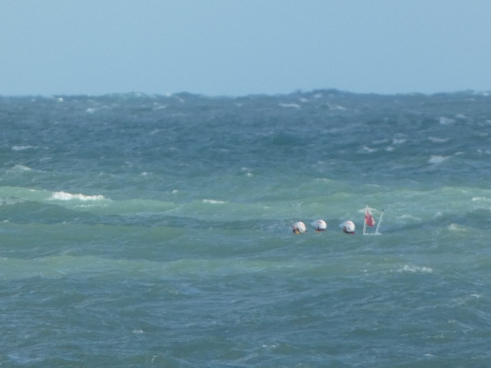 Three RNLI helmets can be seen above the waves
