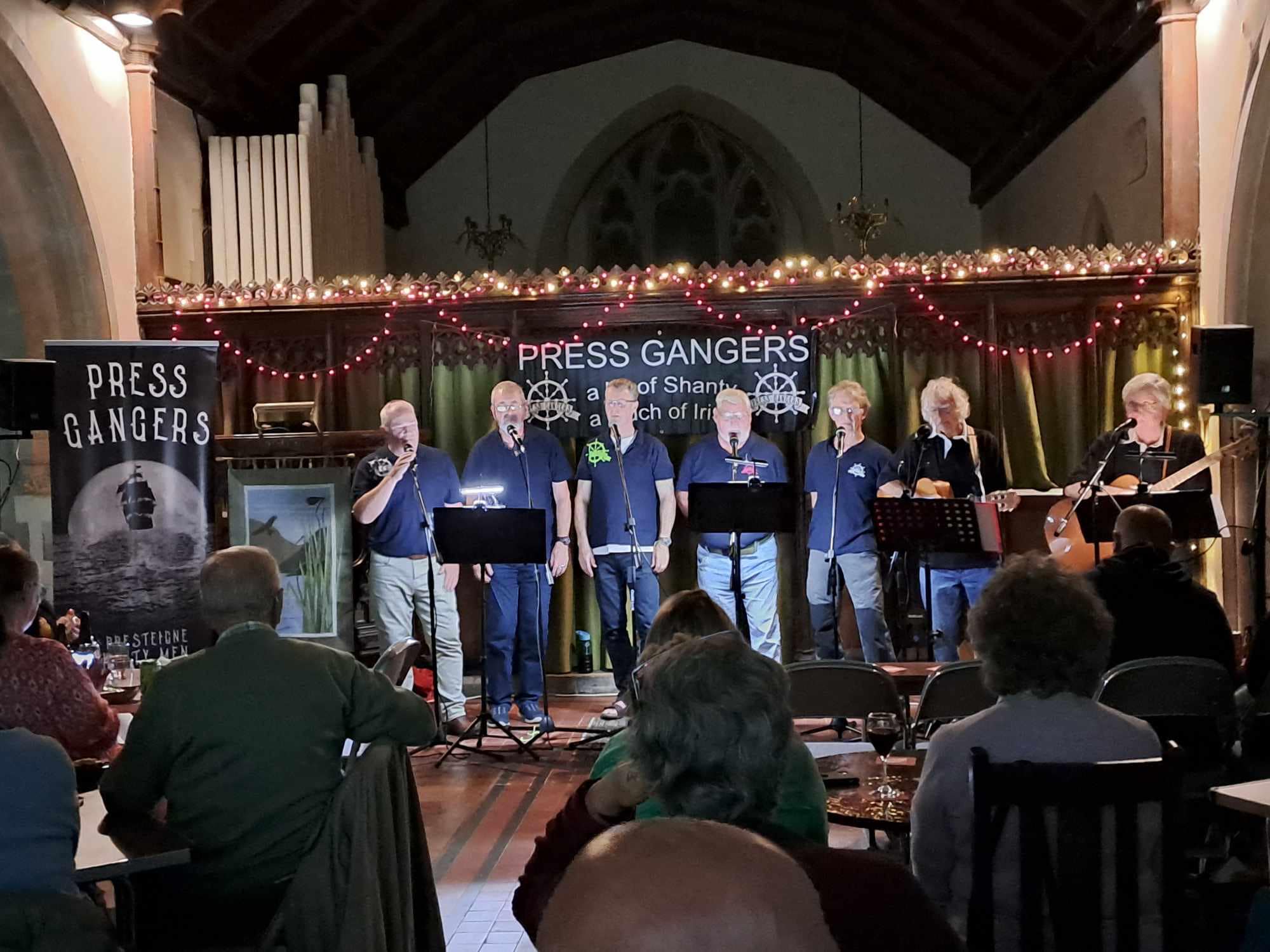 Press Gangers on stage in a church performing with fairy lights in the background.