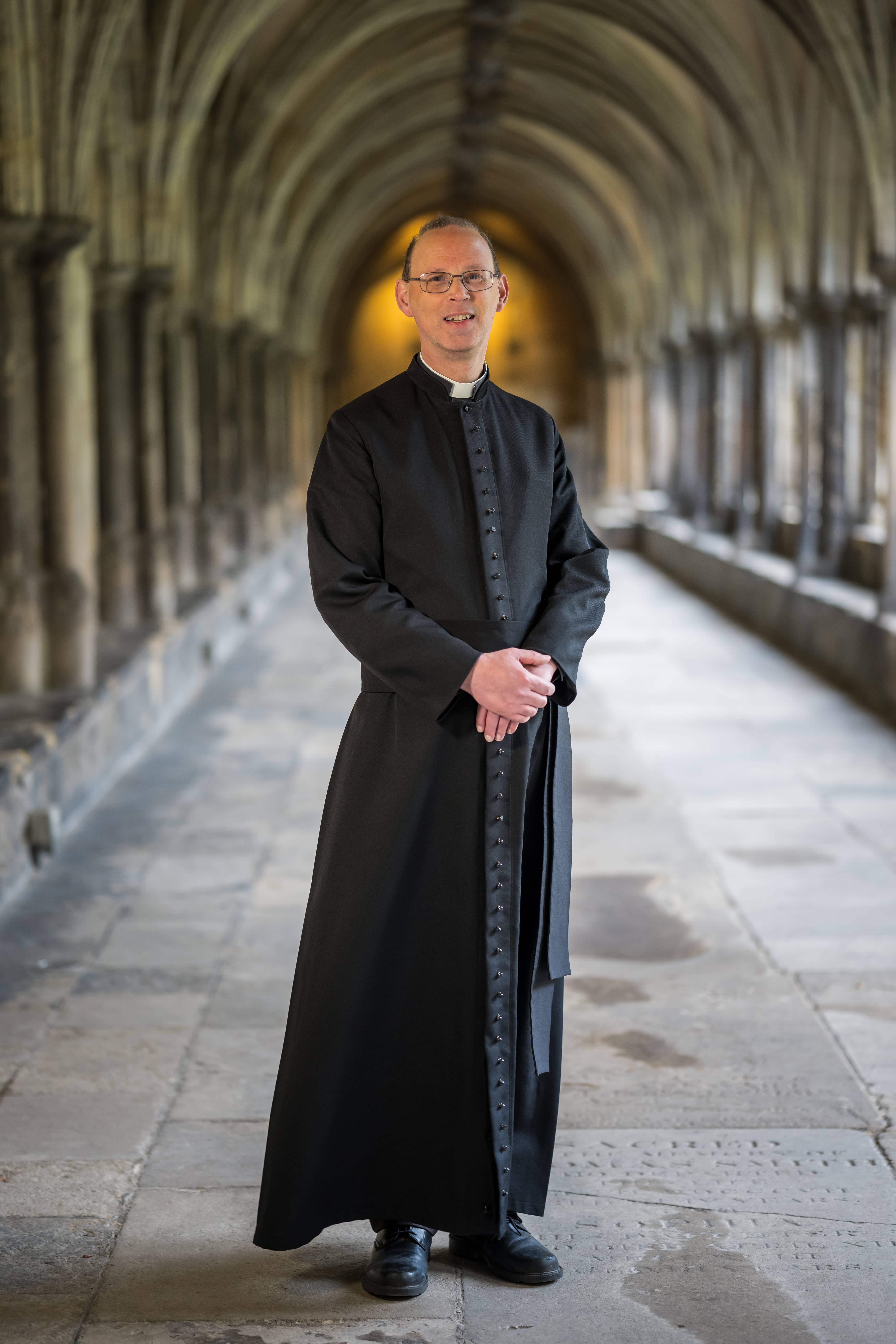 The Dean has brown hair wears glasses and is pictured in the Cathedral.