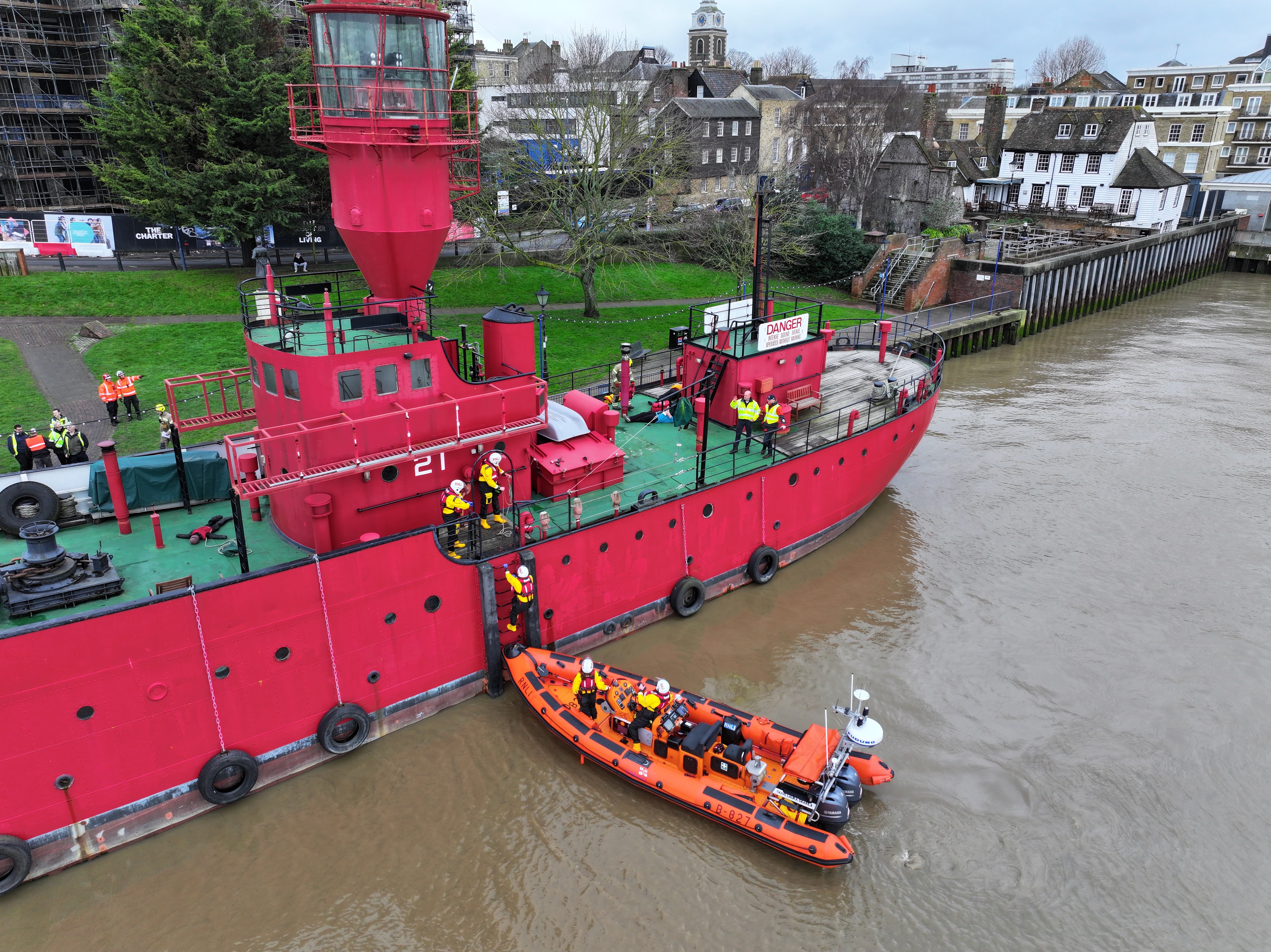 Lifeboat crew climb from orange boat up ladder onto red ship LV21
