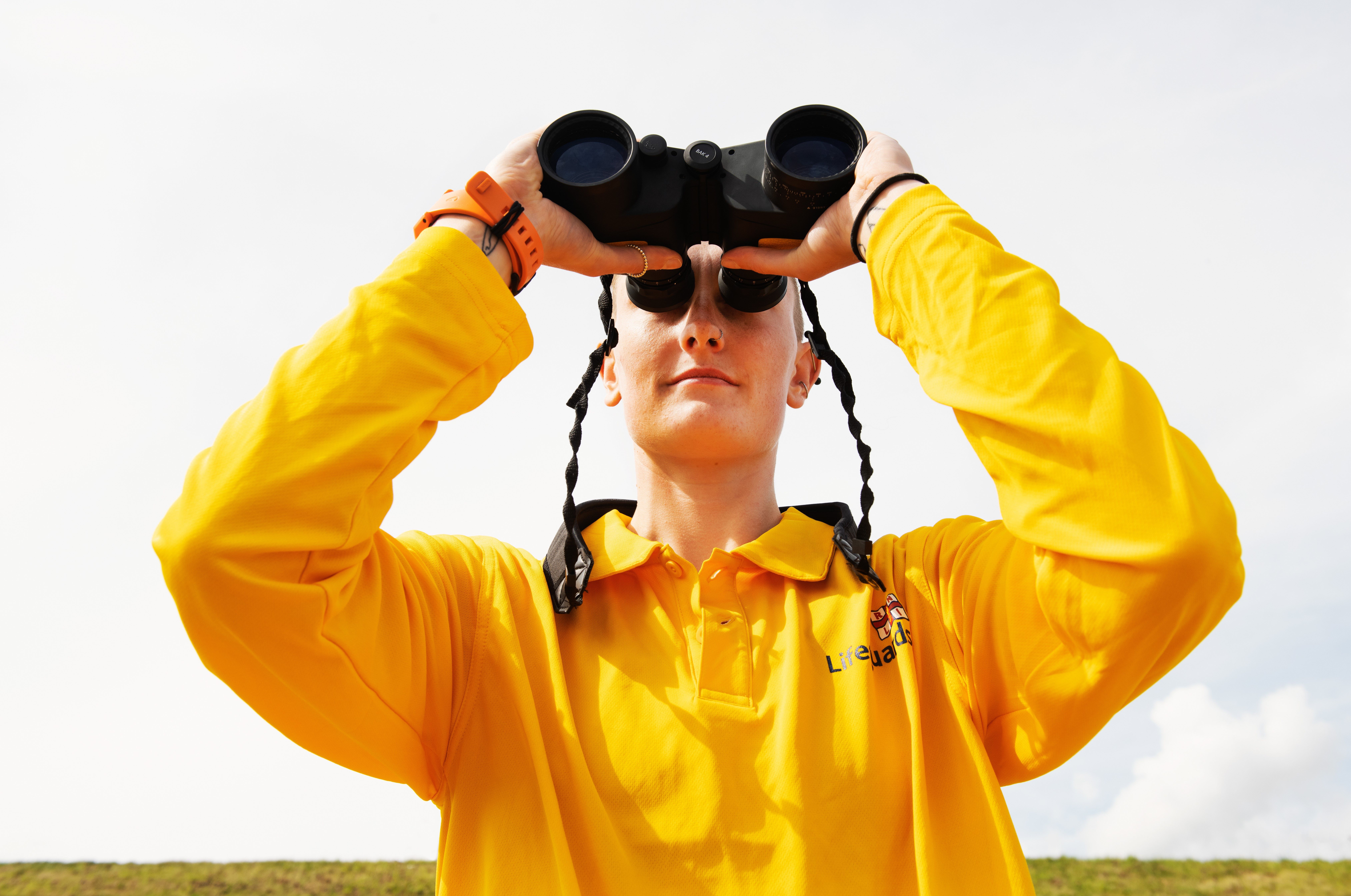 Female lifeguard looks out to sea through binoculars 