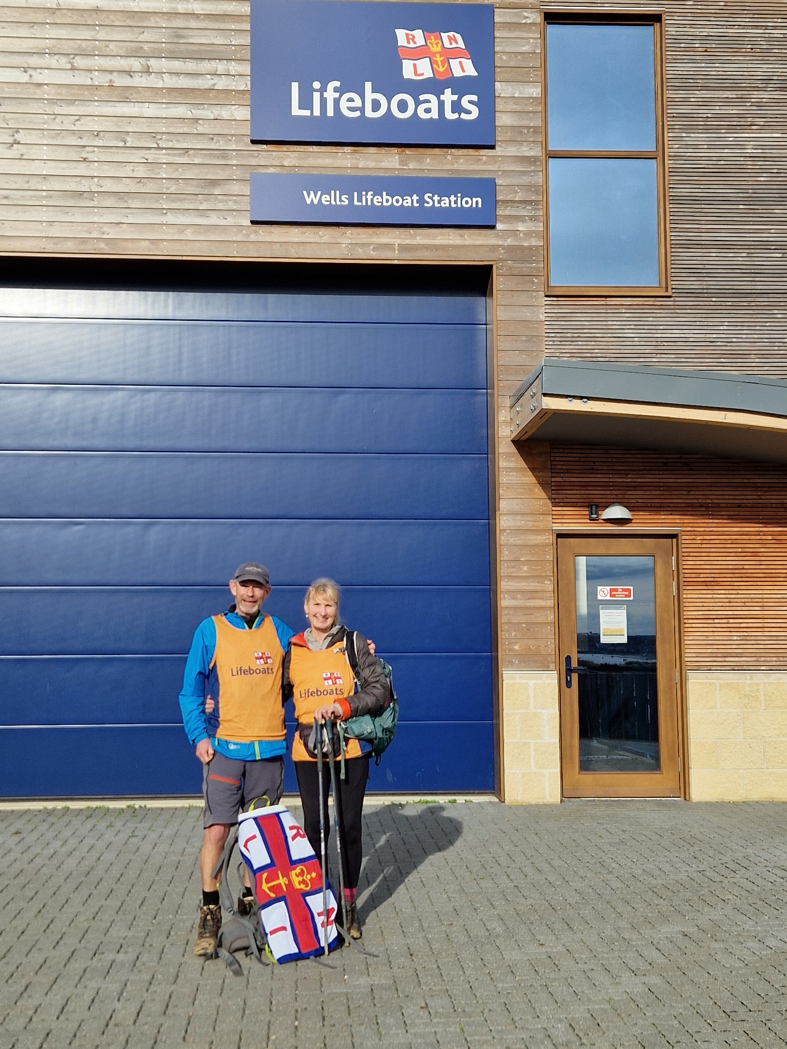 Man and Lady stood in front of Wells RNLI boathouse on a sunny day