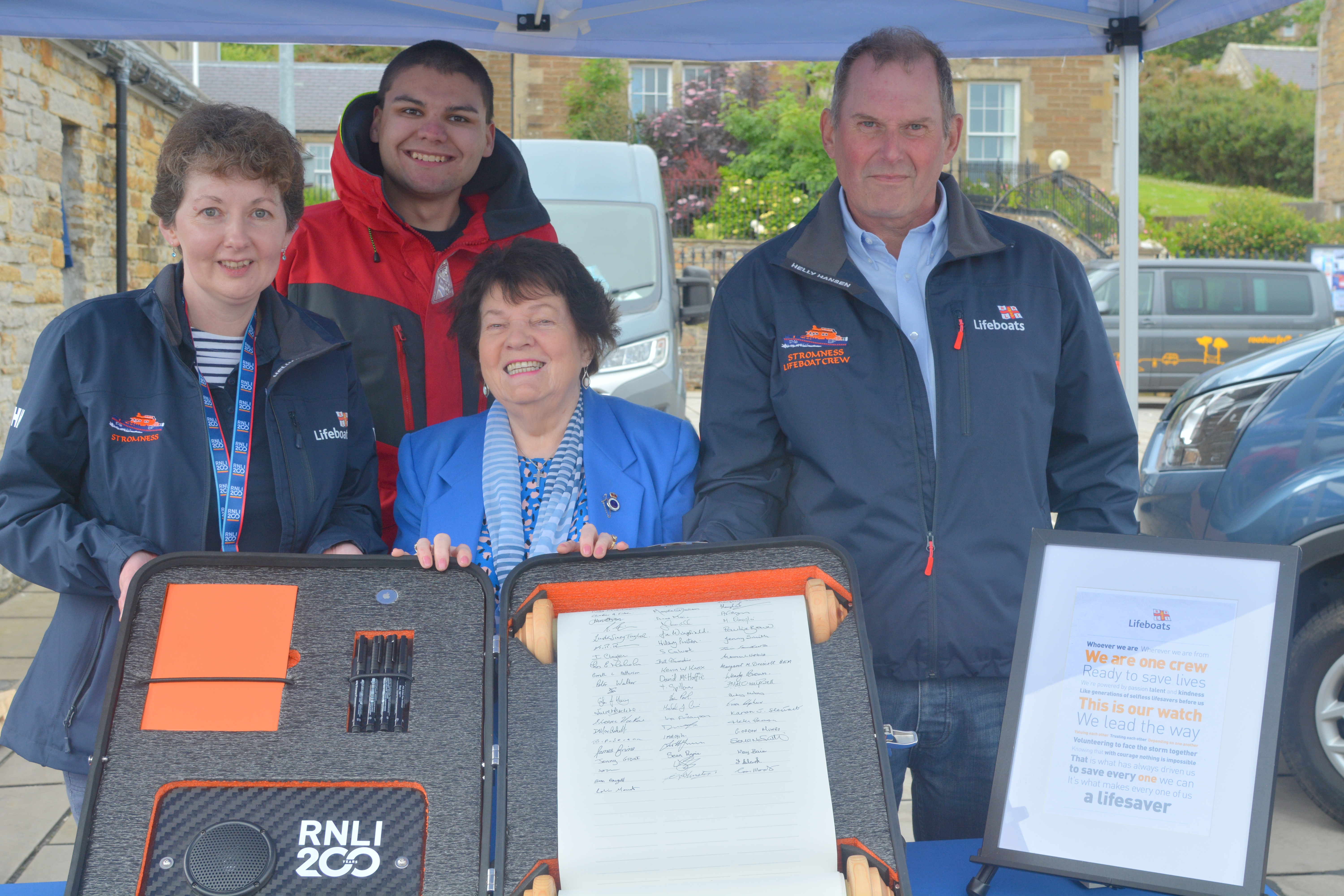 Three Stromness volunteers, plus Chris Smith, with the RNLI200 scroll after the signing