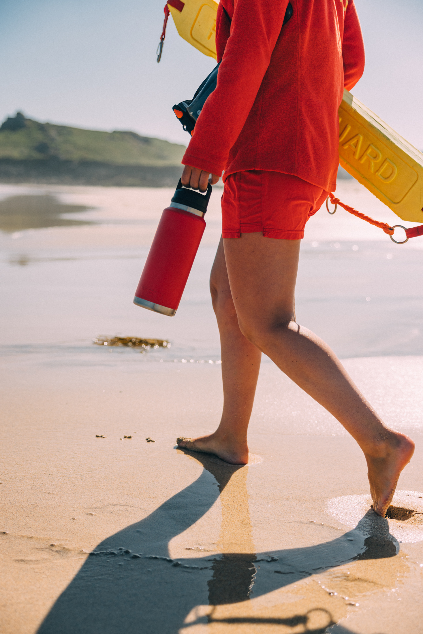 RNLI lifeguard walking along the shore with a Yeti bottle 