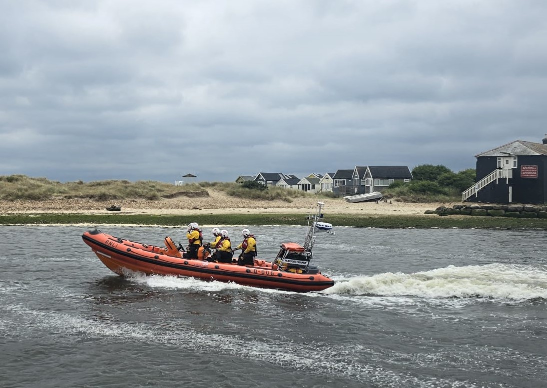 An orange RNLI Atlantic 85 lifeboat with four crew aboard speeding through the Run at Christchurch Harbour