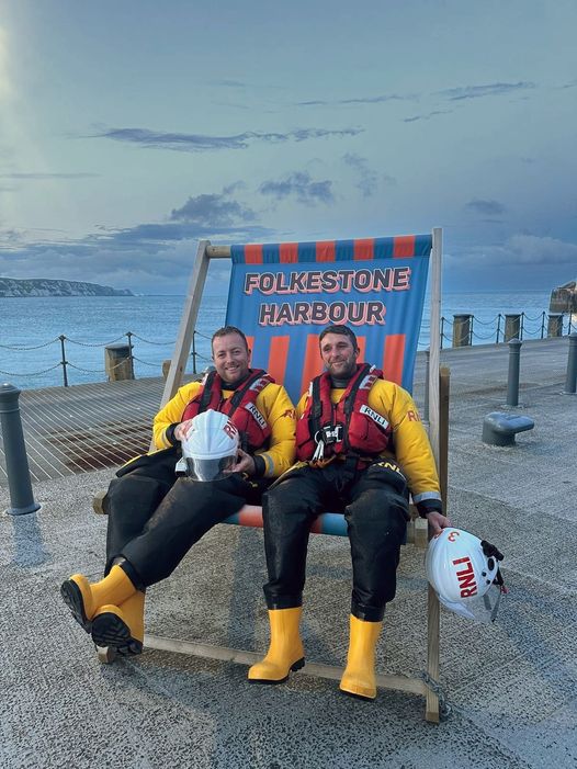 A picture of new Helm Josh Spiers and his friend and colleague Dean Miller sitting on a very colourful oversized deck chair while taking a well earned break at Folkestone Harbour after a shout