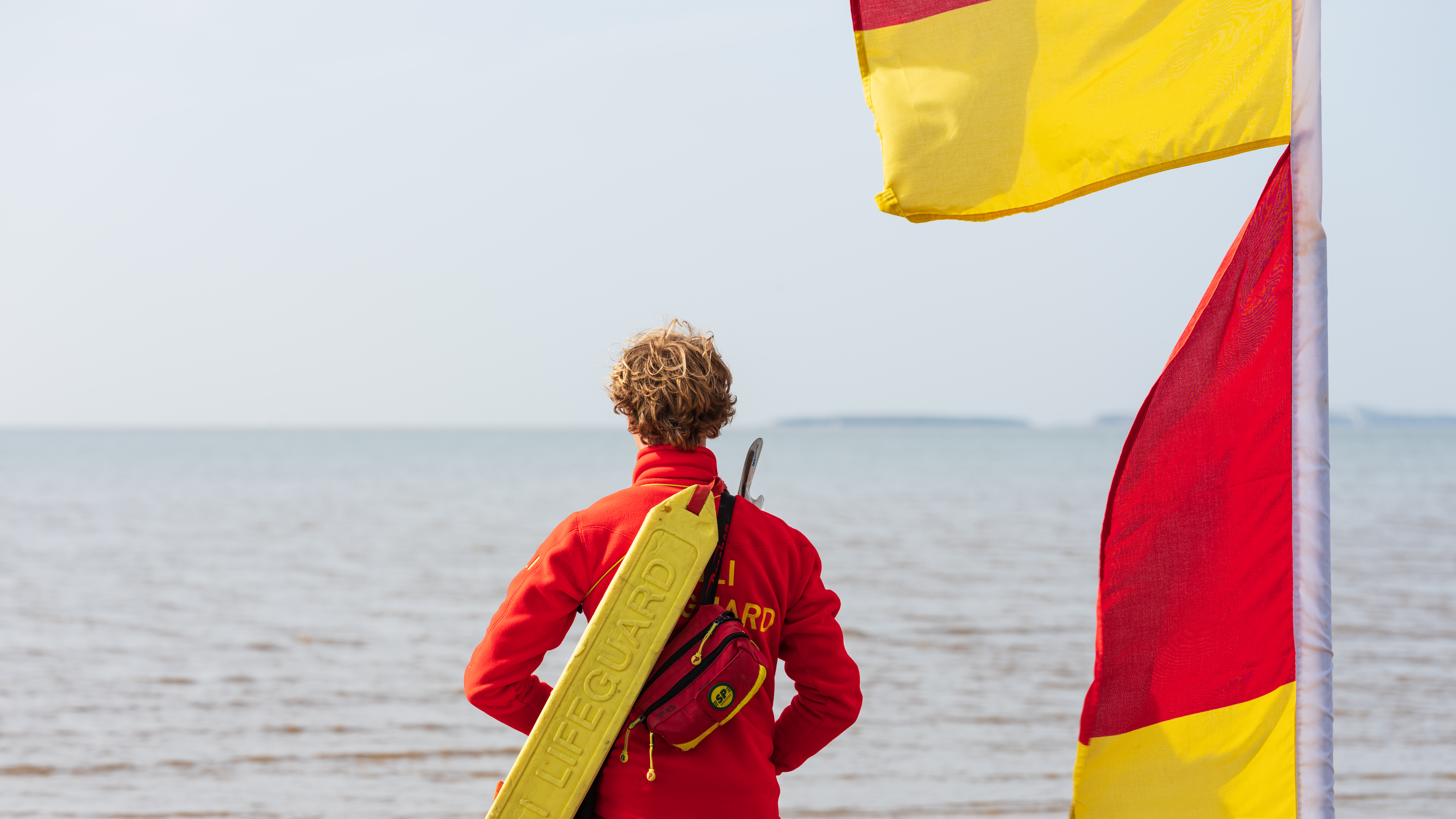 Lifeguard to the left of the red and yellow flag looking out to sea