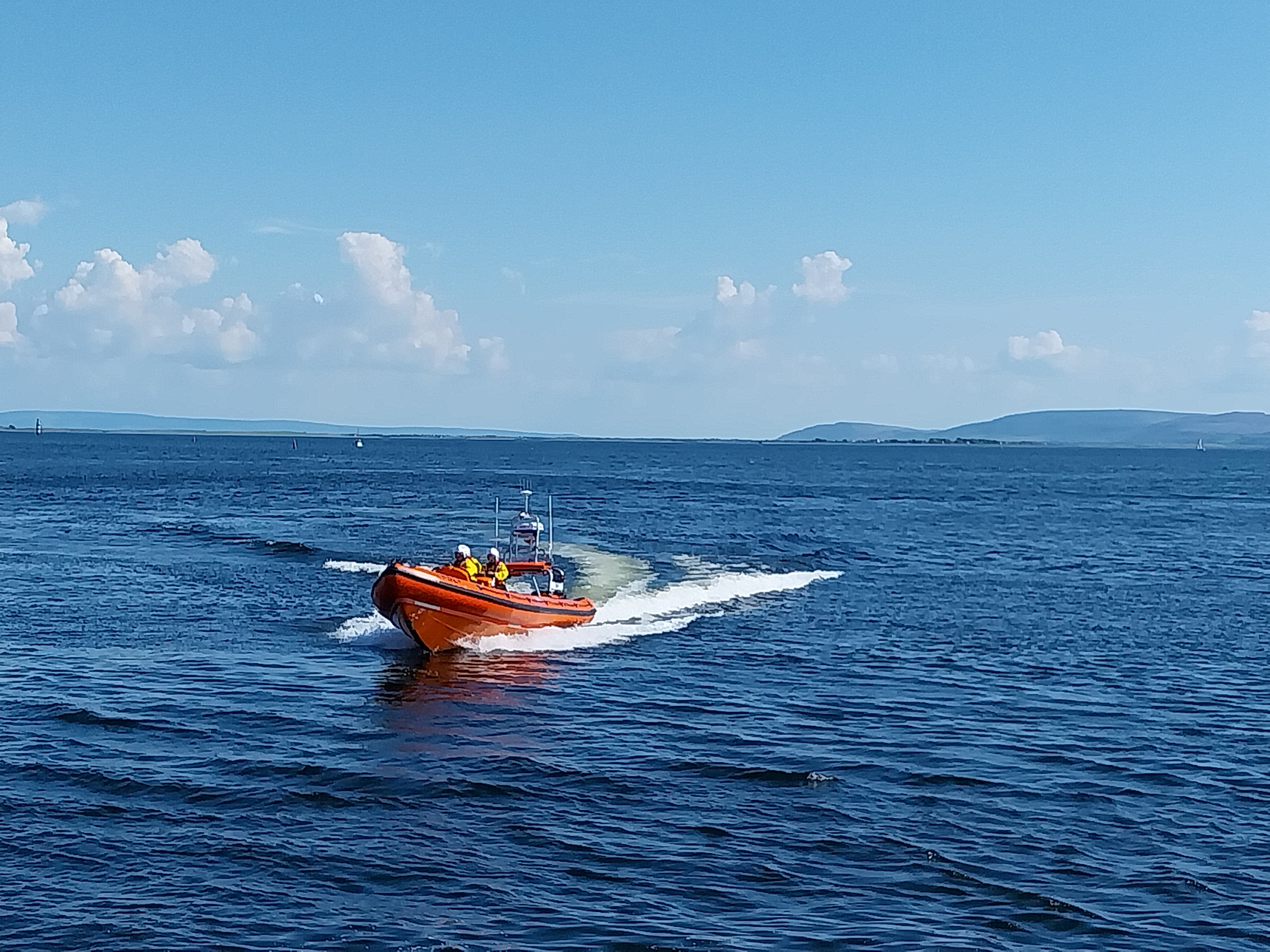 Inshore lifeboat on open water with a wake visible behind on an exercise on Galway Bay. Sunny day with blue skies