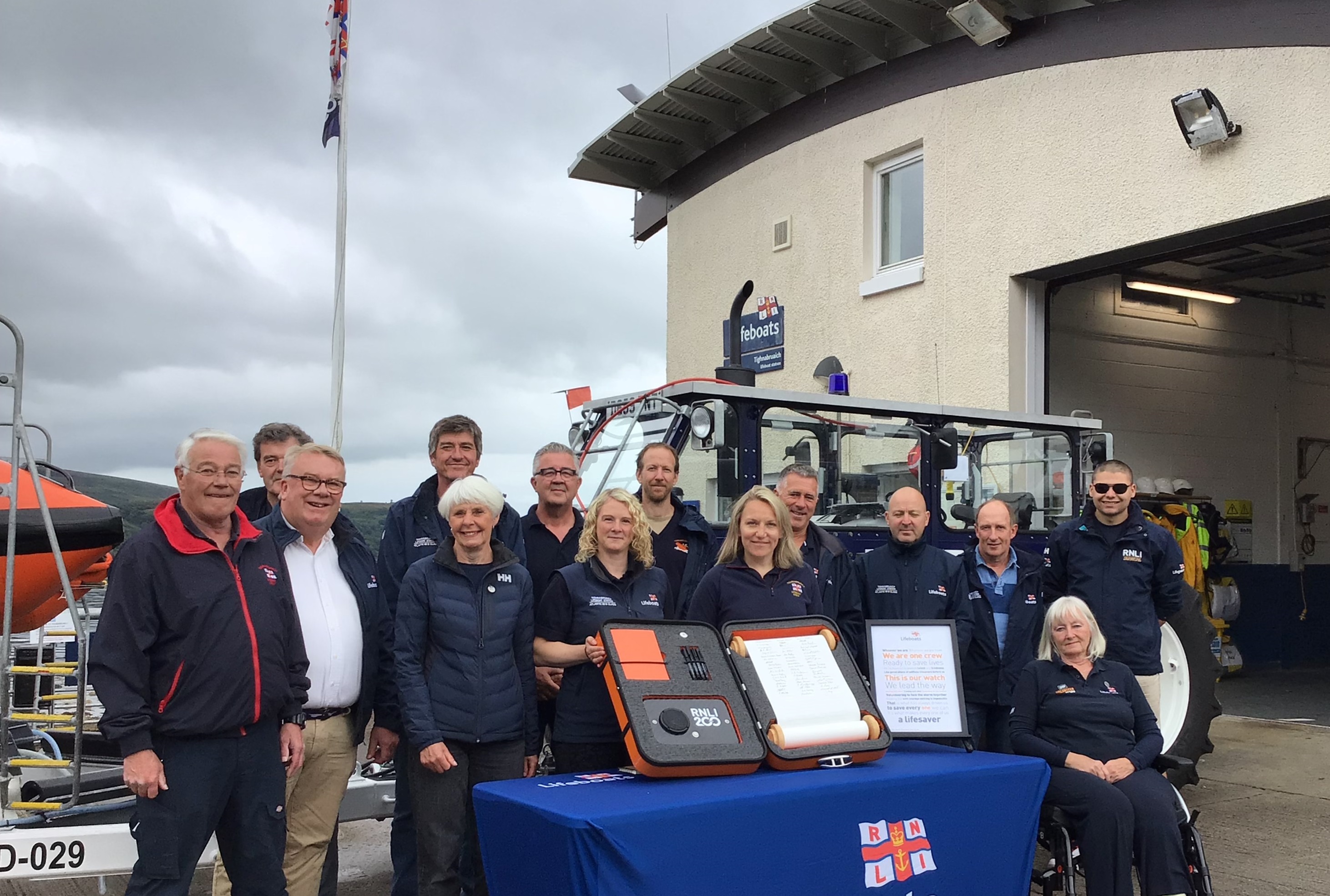 Crew and fundraising volunteers gathered for the signing of the scroll with the station in background