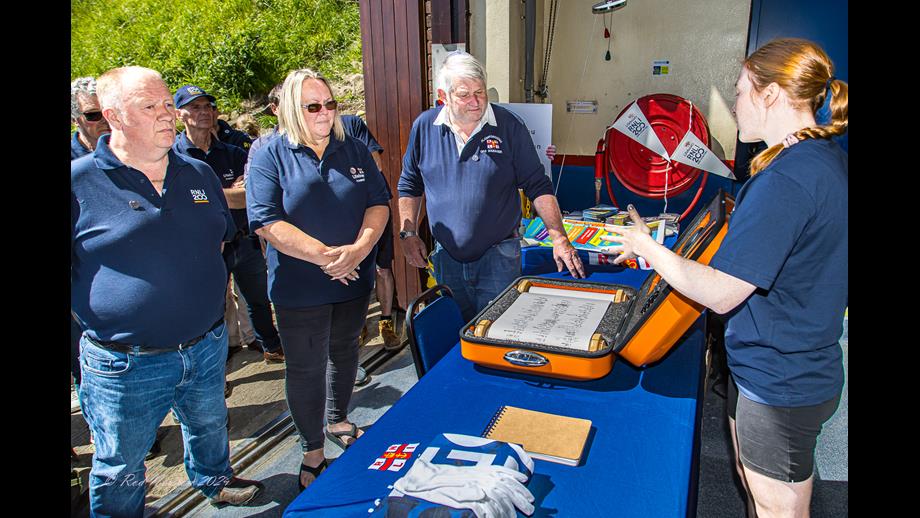RNLI200 Scroll delivered to Flamborough Lifeboat Station Three signatories standing at a table which has the open scroll case. Charlotte at the back of the table speaking.