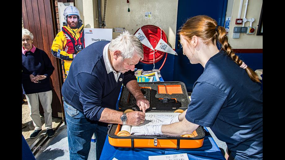 RNLI200 Scroll delivered to Flamborough Lifeboat Station David Freeman bending don over the table signing the scroll which is inside an open case.