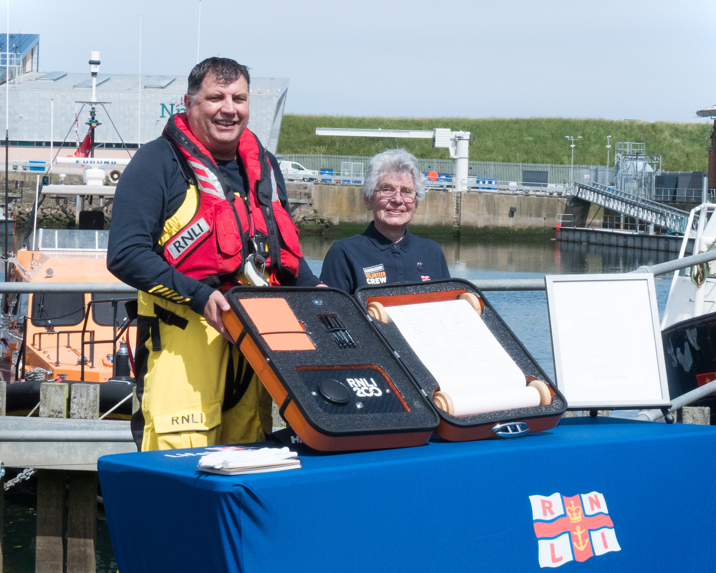 Peter Walker and Margaret Driscoll stand with the RNLI 200th anniversary scroll, the Eyemouth lifeboat in the background