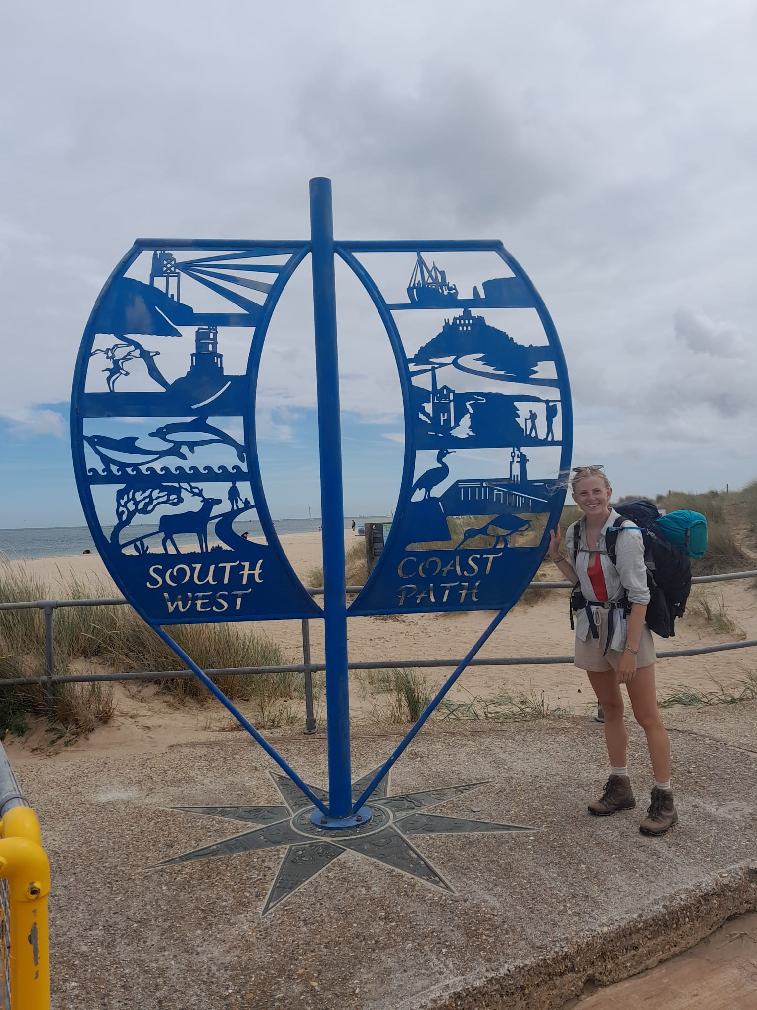 Woman stands at sign for South West Coast Path.