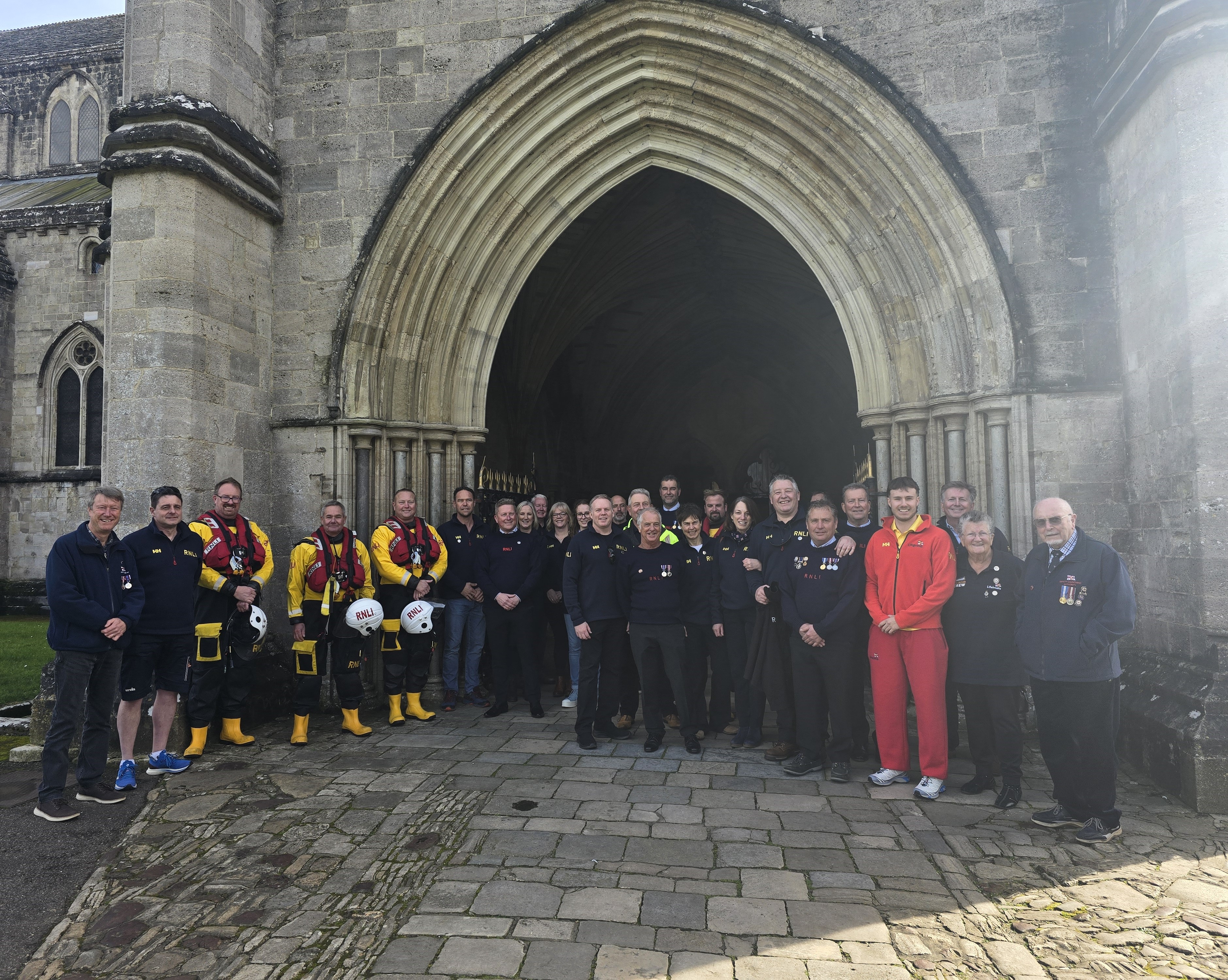 A group of Mudeford RNLI crew members outside the stone archway entrance to Christchurch Priory