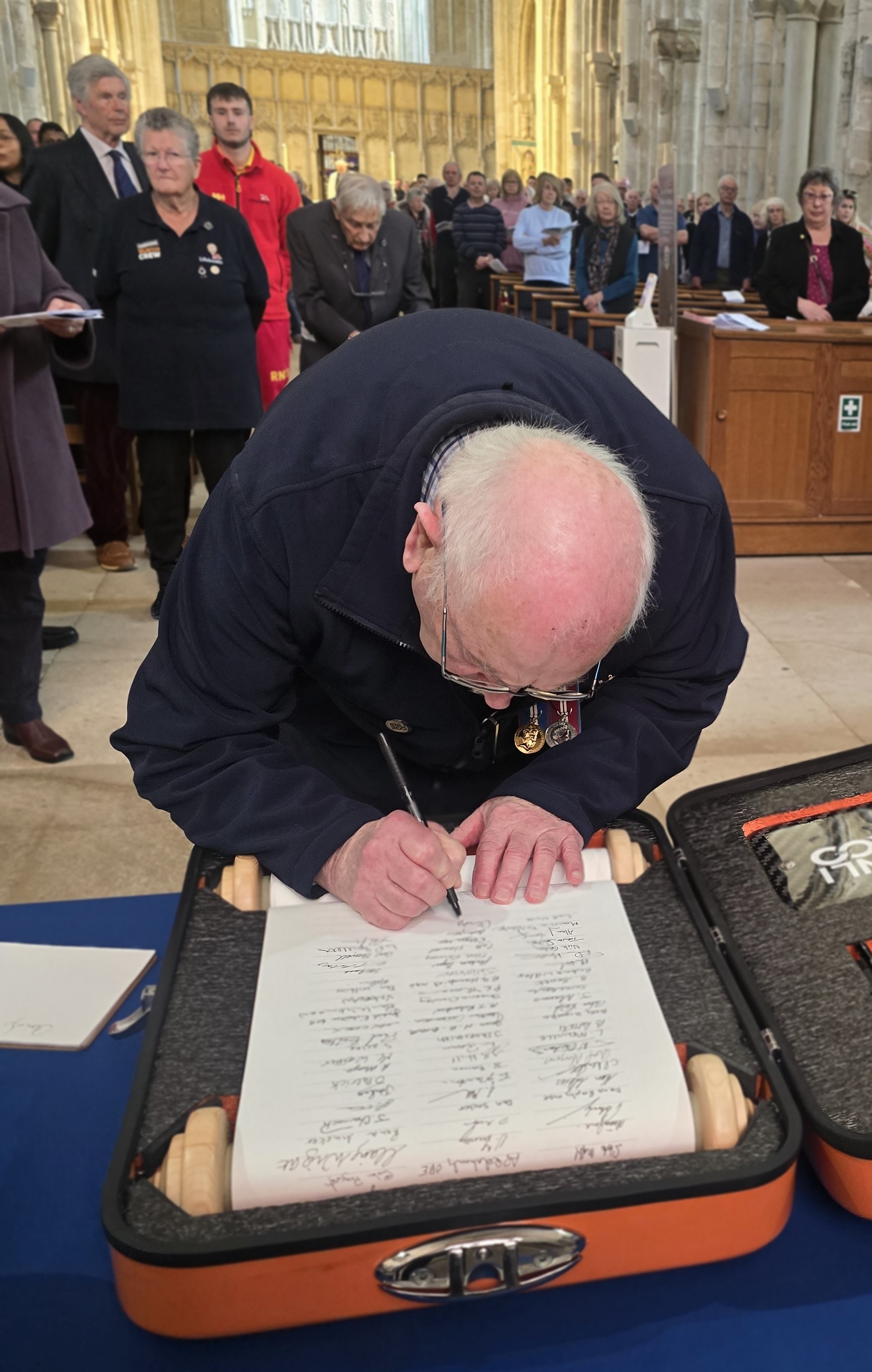 A gentleman leans across a table to sign the RNLI 200th Anniversary Scroll