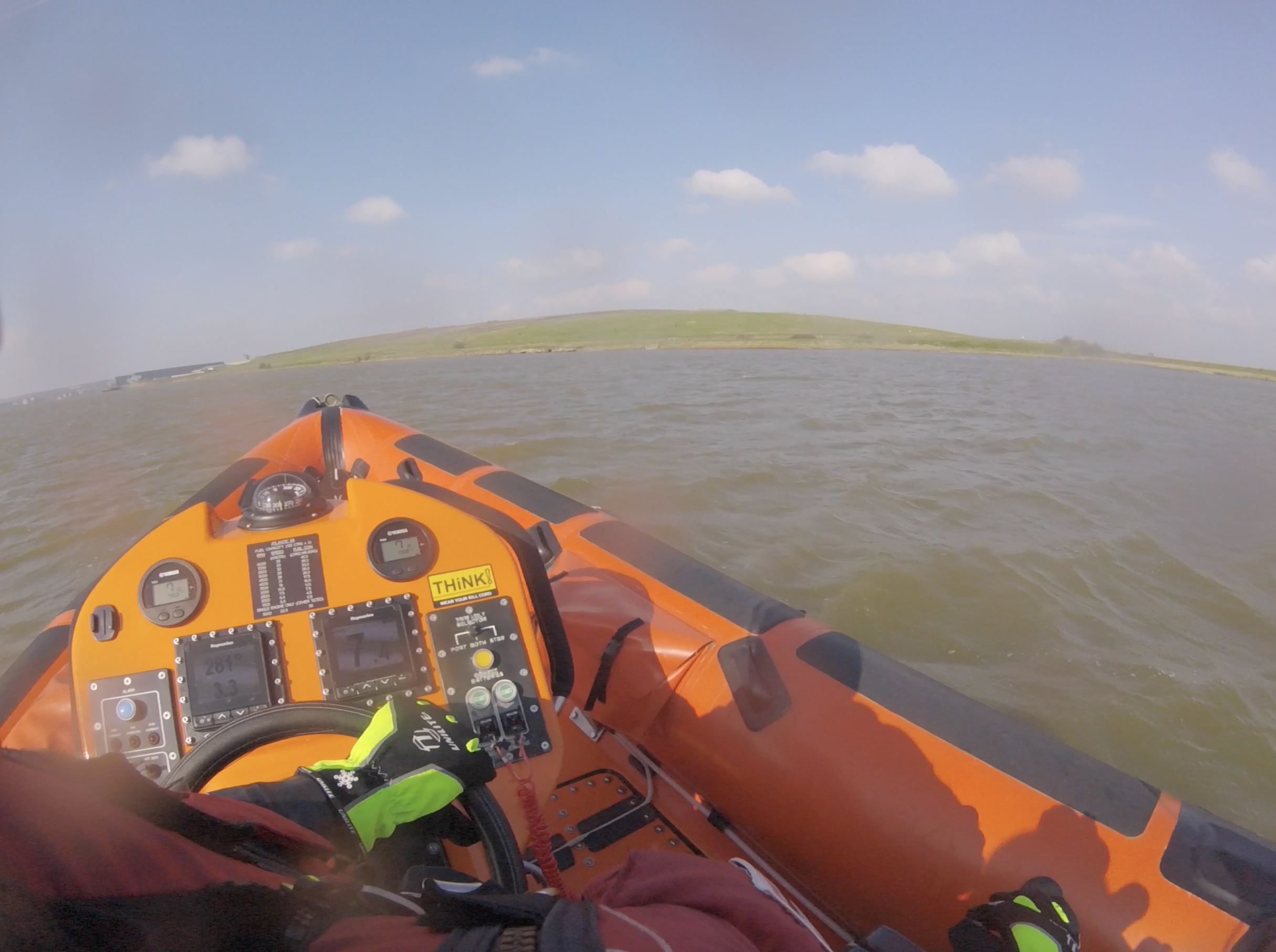Orange lifeboat pointing shoreside facing a landfill site