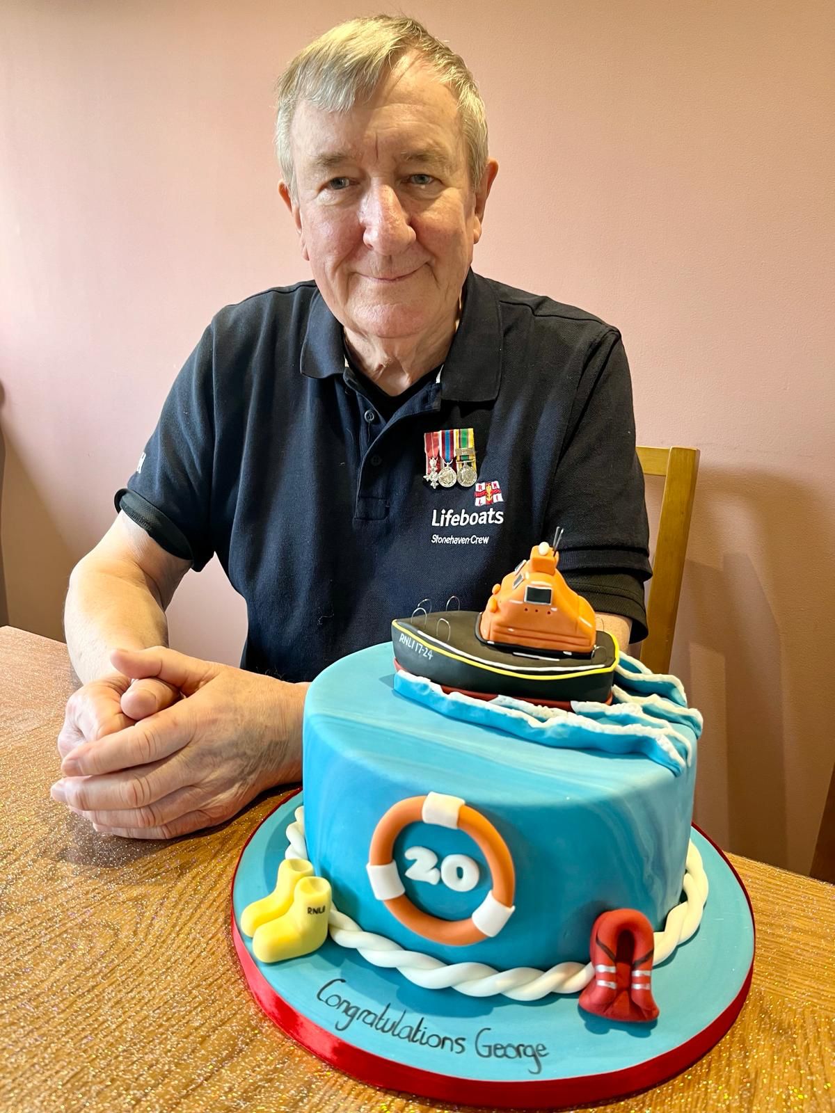 George with his celebration cake which has a lifeboat on the top, yellow wellies, life jacket and blue icing to represent the sea
