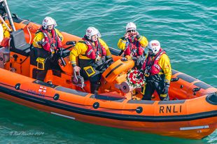 View from clifftop of lifeboat with crew holding wreath
