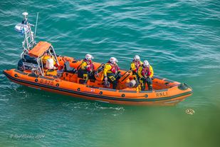 View from the clifftop of lifeboat and wreath floating on the water.