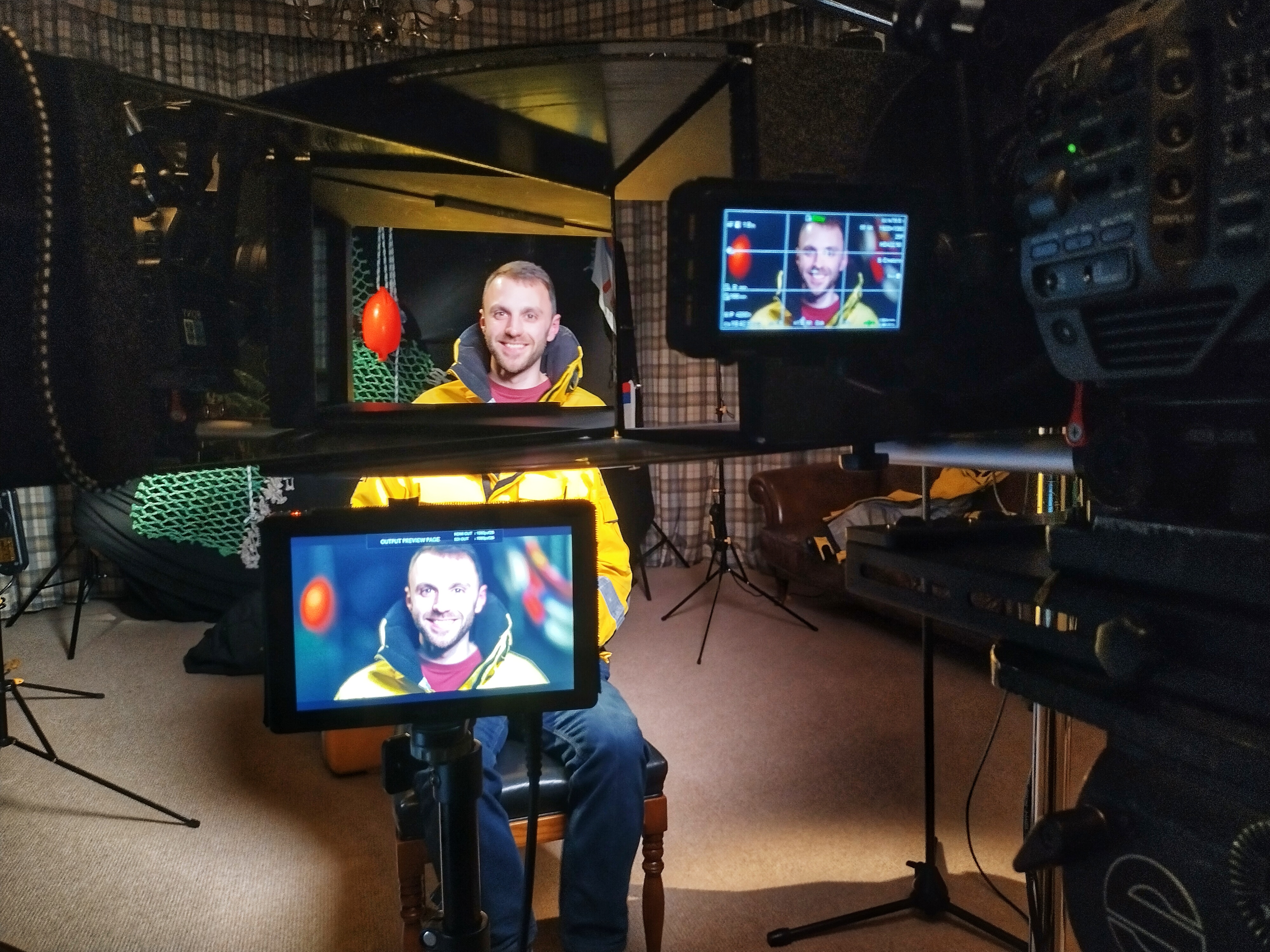 Crew member sat behind film camera with face appearing on multiple screens