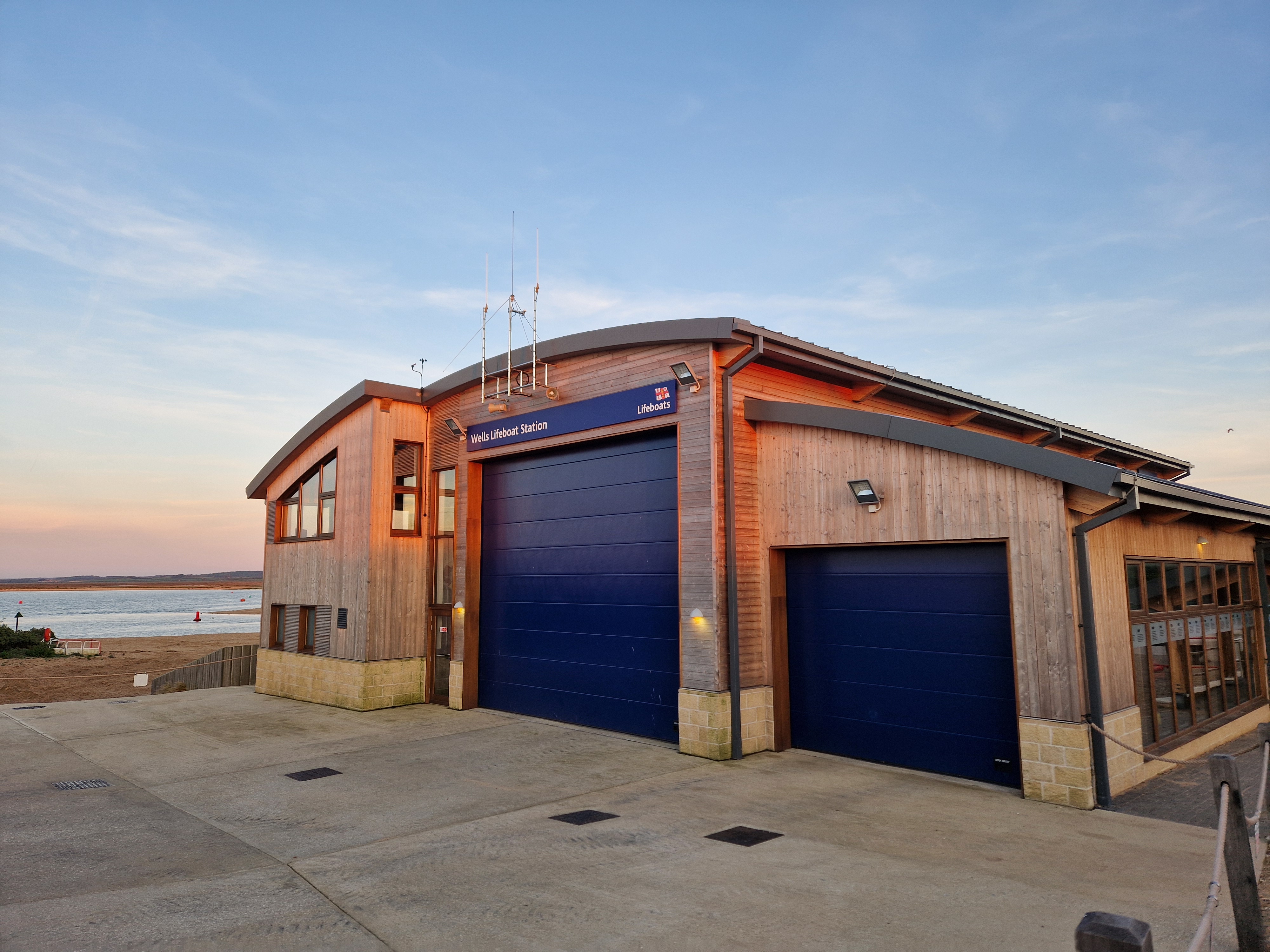 Wells RNLI boathouse with the setting sun and the sea behind