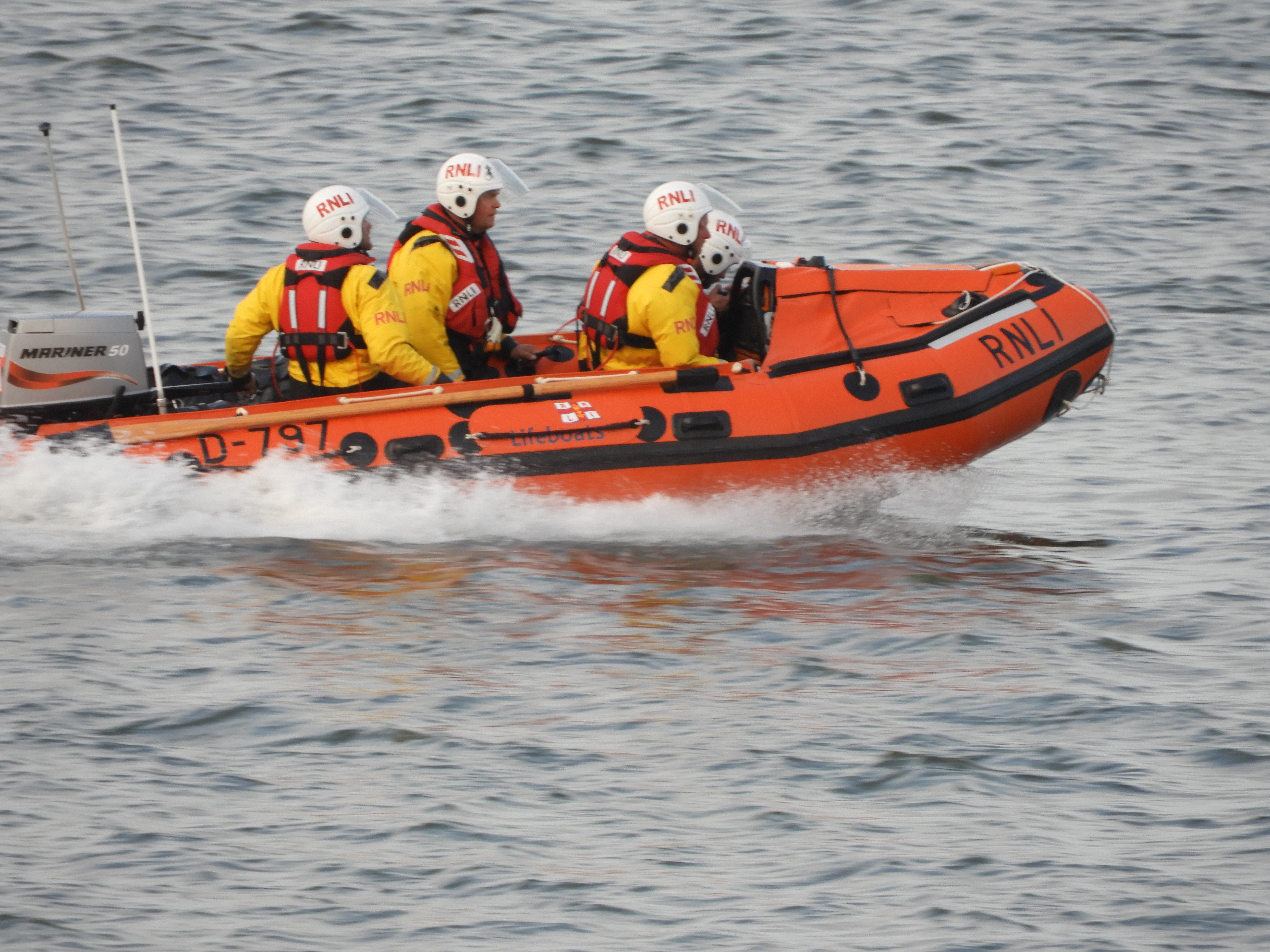 D-Class lifeboat in sea with spray from it and 4 RNLI crew members