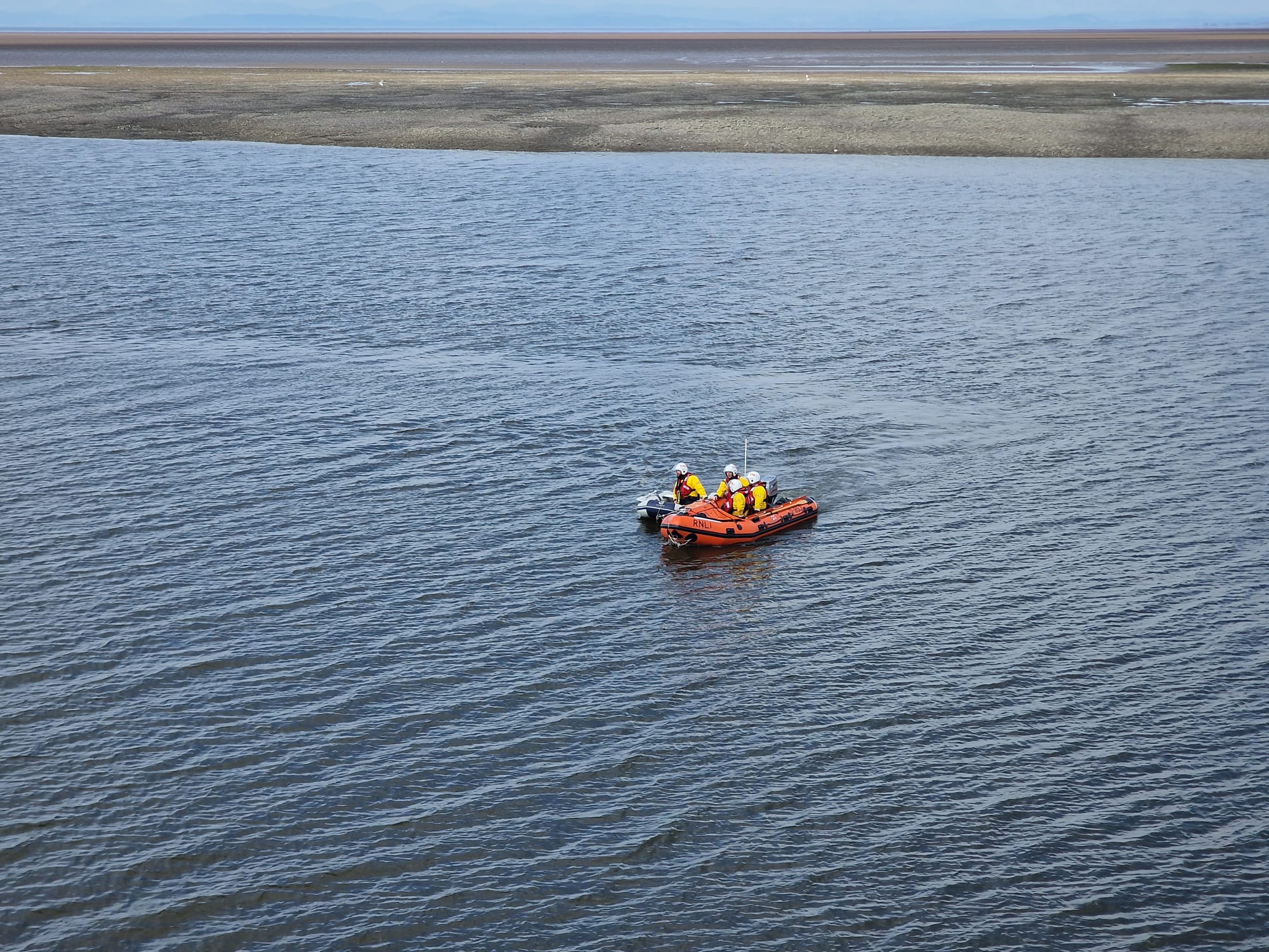A D-class lifeboat towing a light grey rib, attached to its starboard side.