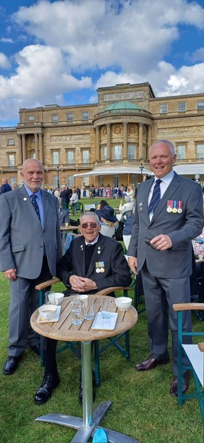 Three men in suits and medals at a table outside Buckingham Palace