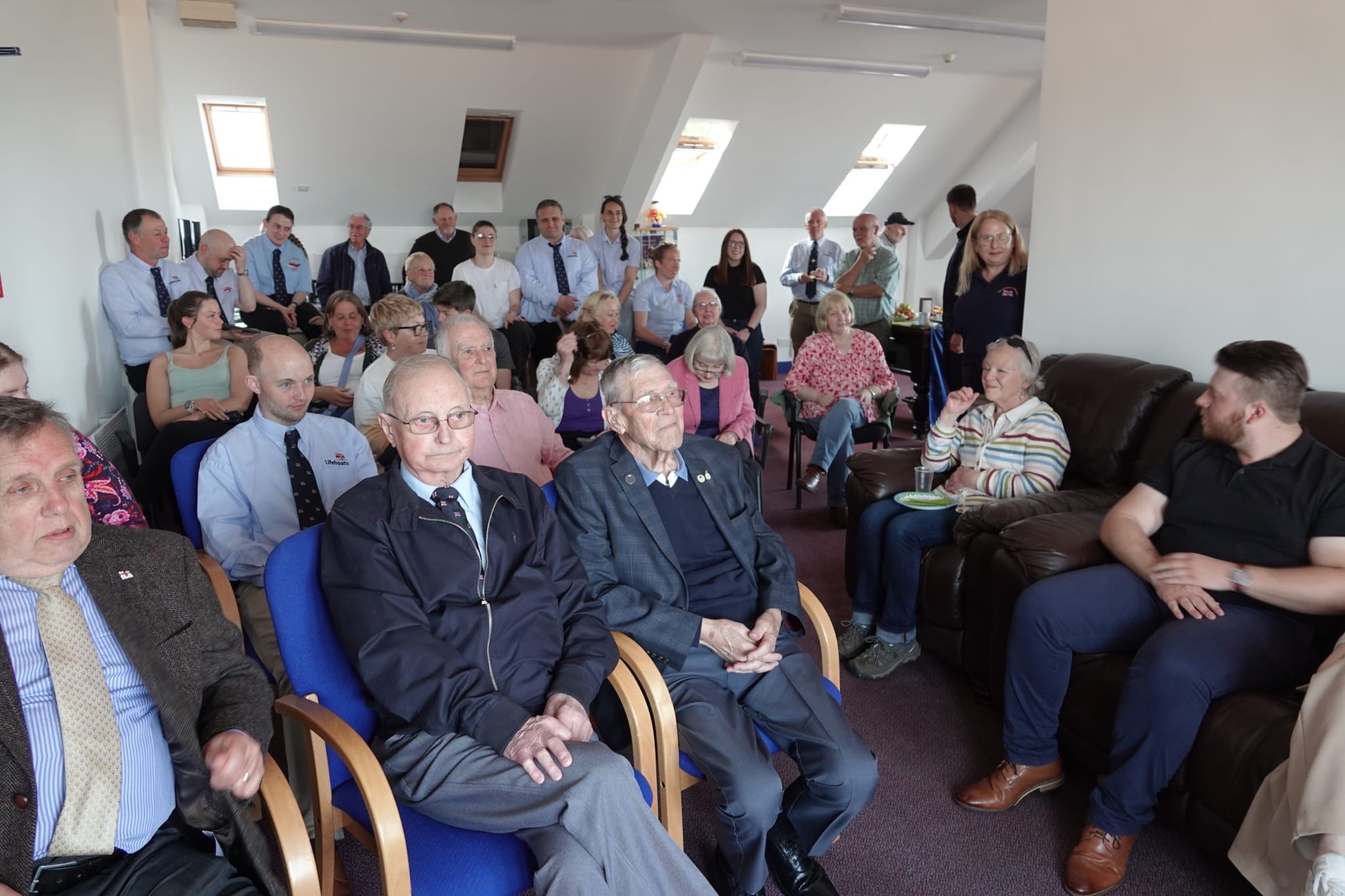 Volunteers sit in rows in smart dress at Cullercoats lifeboat station 