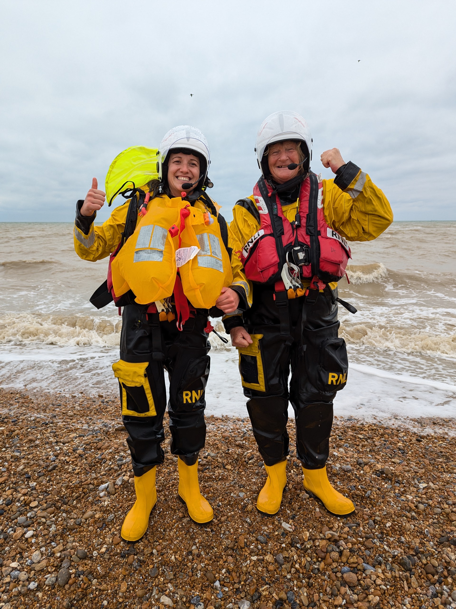 Mihaela and Sarah from Littlestone RNLI in full yellow and black RNLI drysuits giving the thumbs up after their successful trips afloat