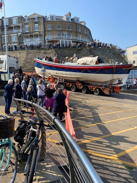 A line of people watching heritage lifeboat being driven away on a lorry.
