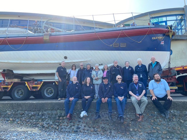 Long line of people in RNLI branded clothes alongside heritage lifeboat.