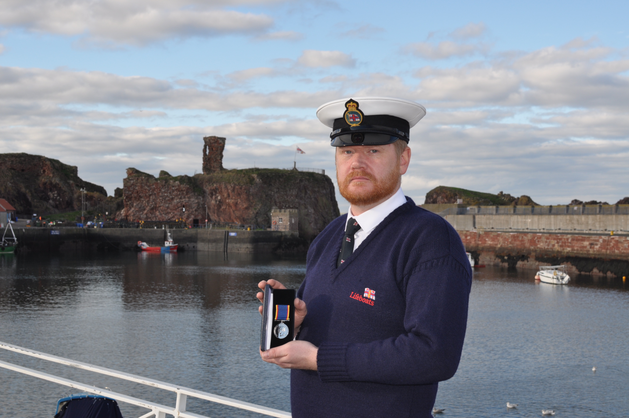 Man with medal in front of harbour.