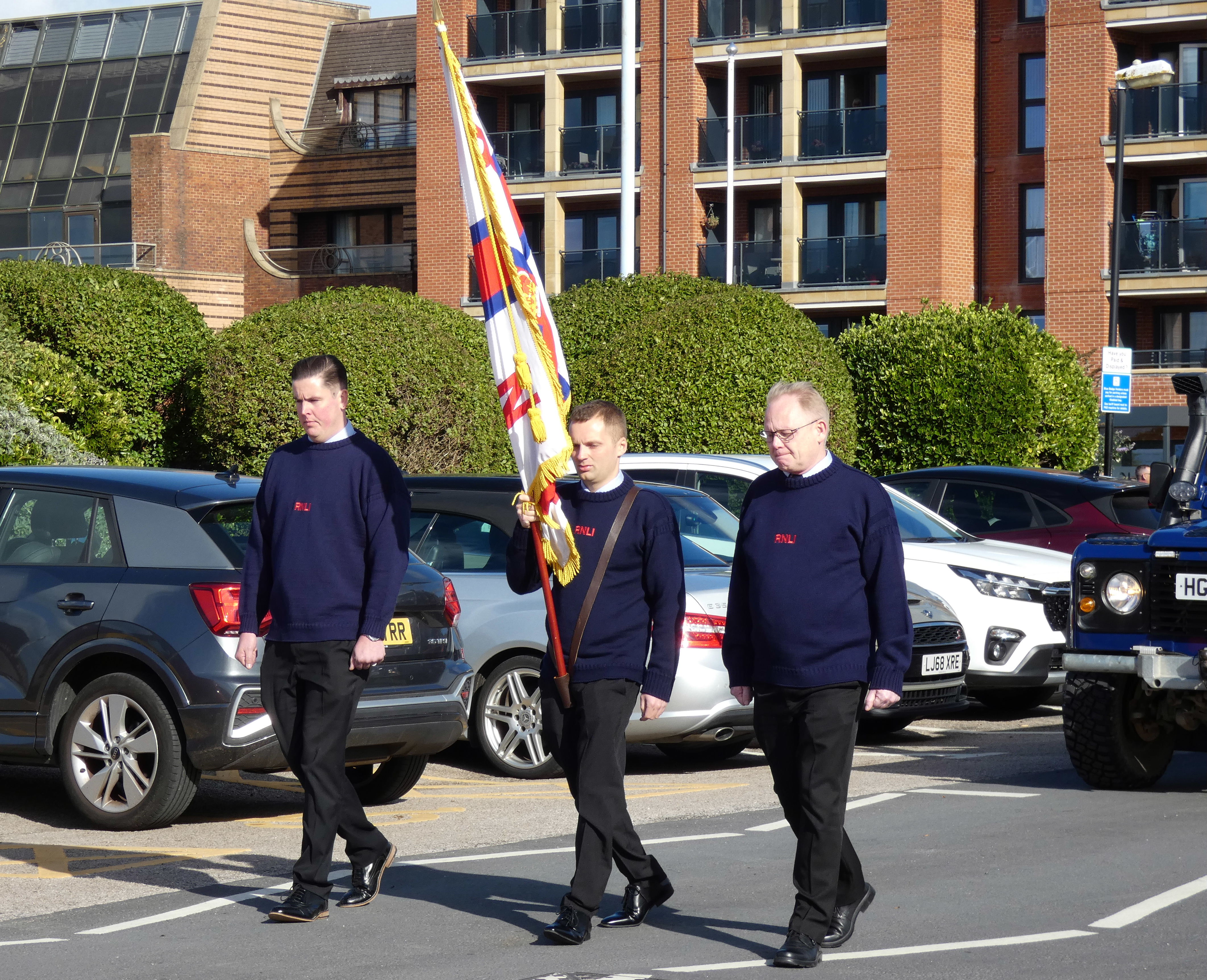 The RNLI ensign is carried by a crewmember flanked by two others