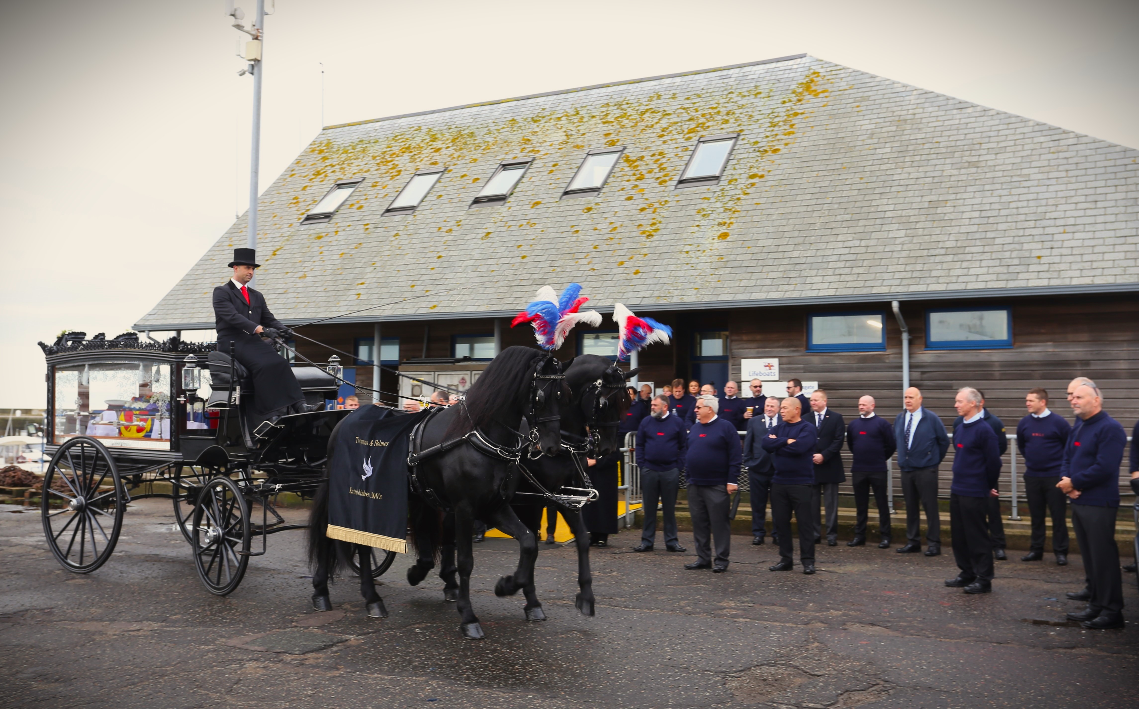 A horsedrawn hearse with crew standing by. 
