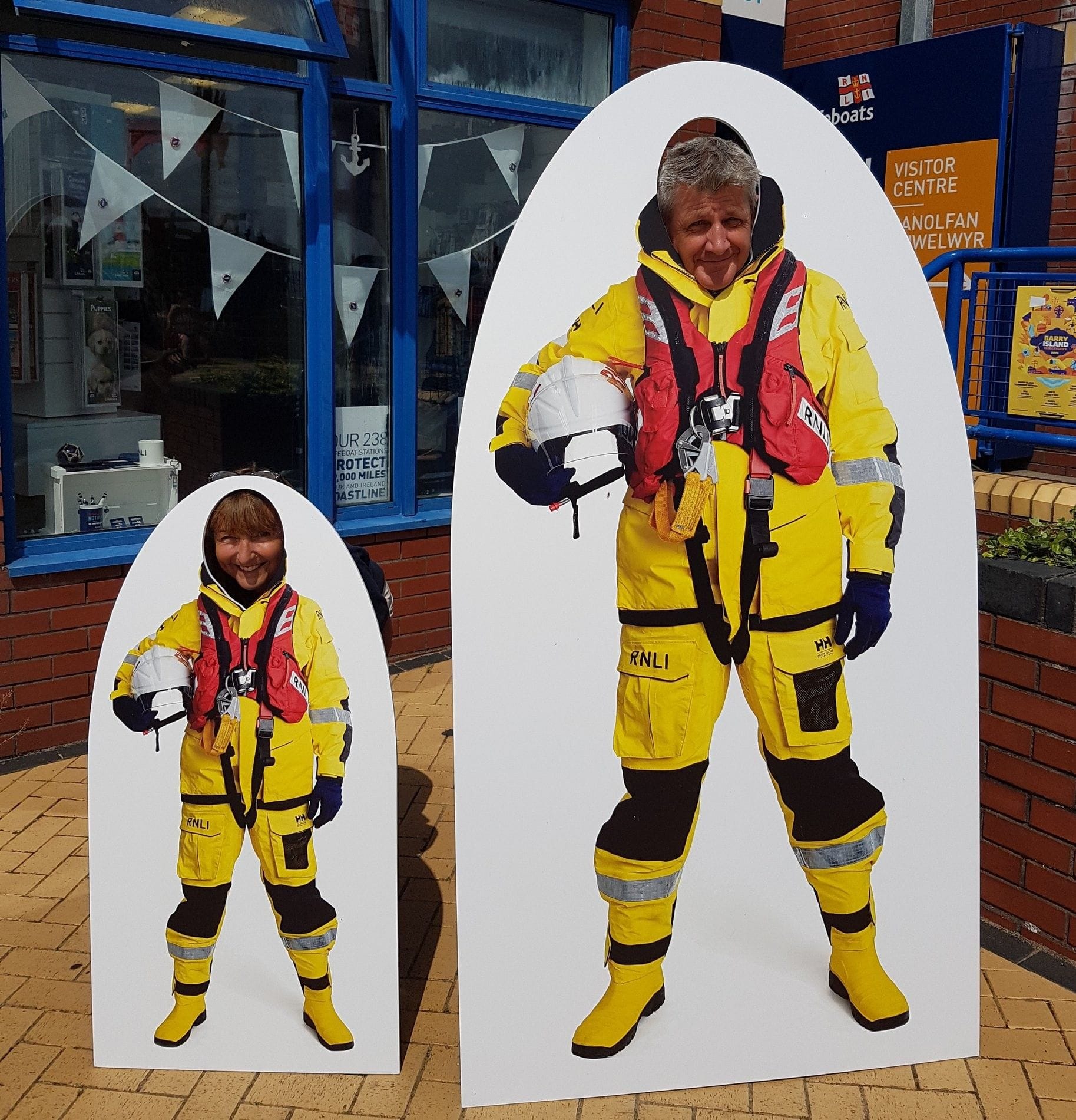 Photo of two volunteers with their heads poking through an image of a person in full volunteer kit