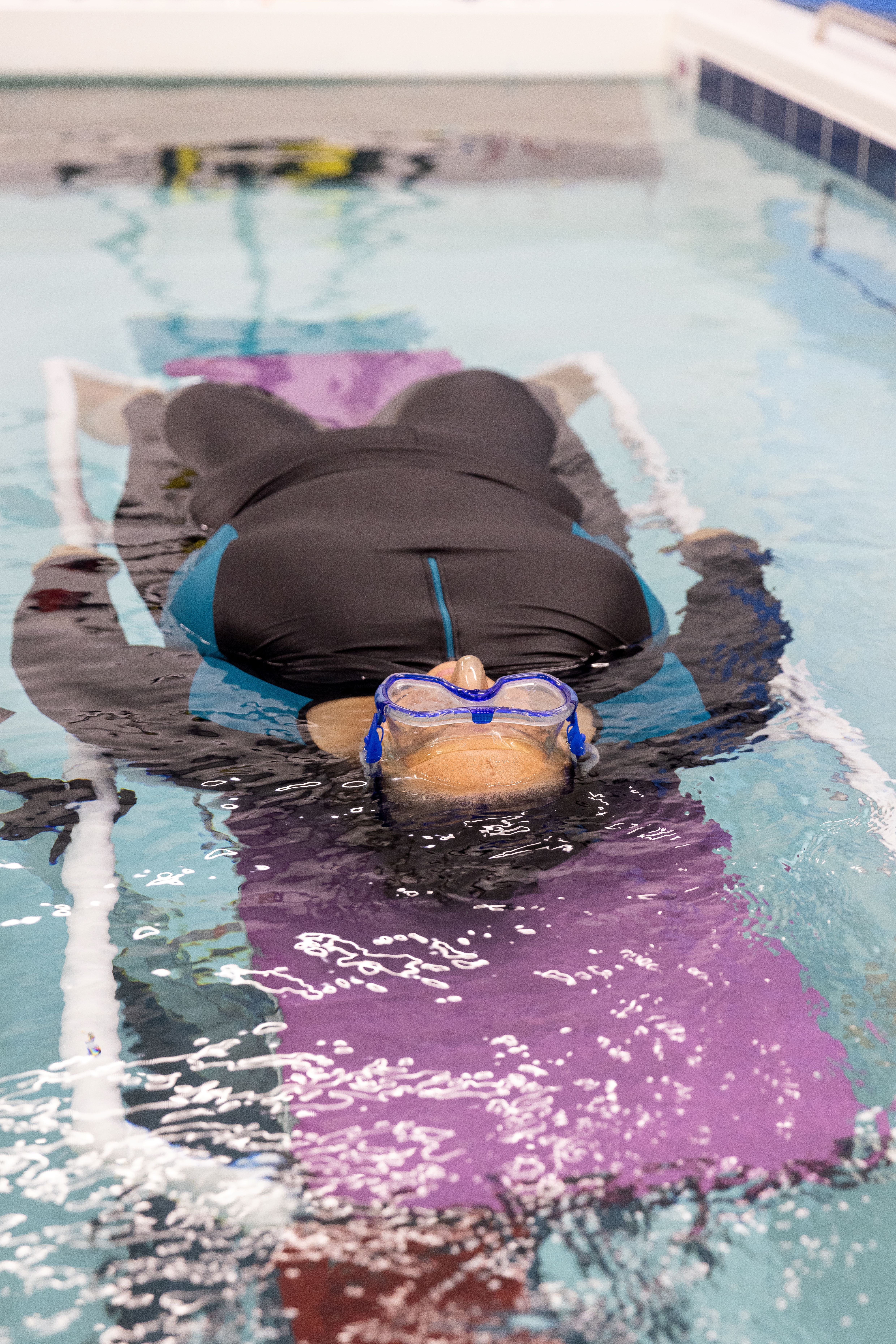 A female participant wearing a diving mask, lying on her back on a stretcher and partially submerged in water.