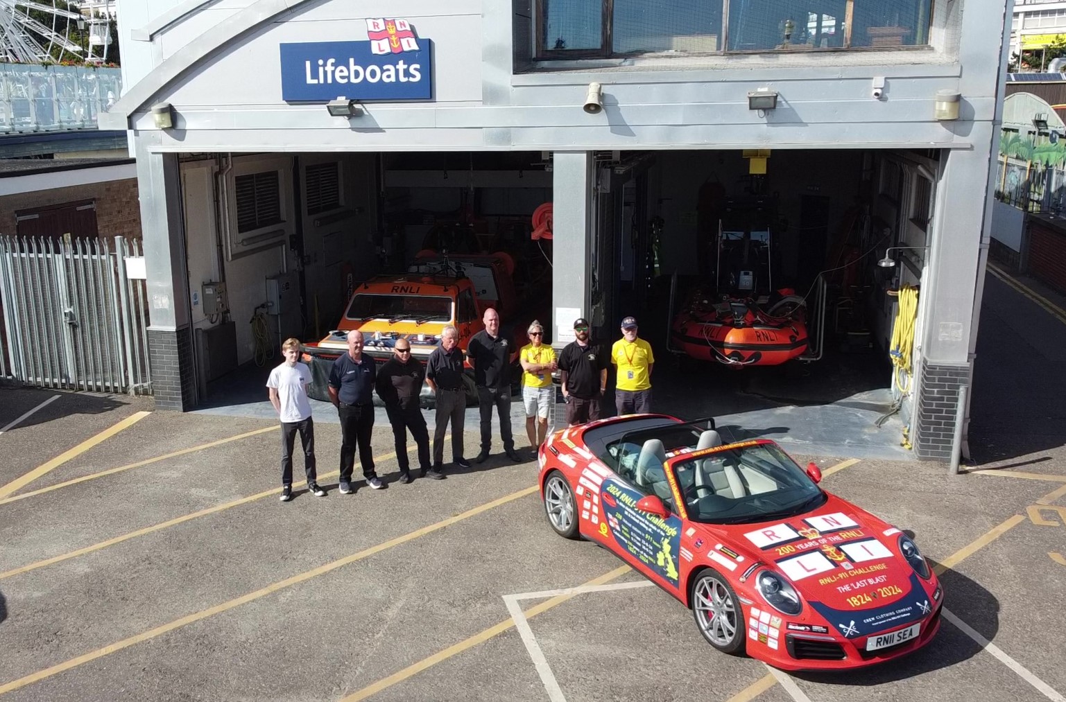 Belinda and James with Southend RNLI volunteers standing next to the Porsche 911 in front of the lifeboat station