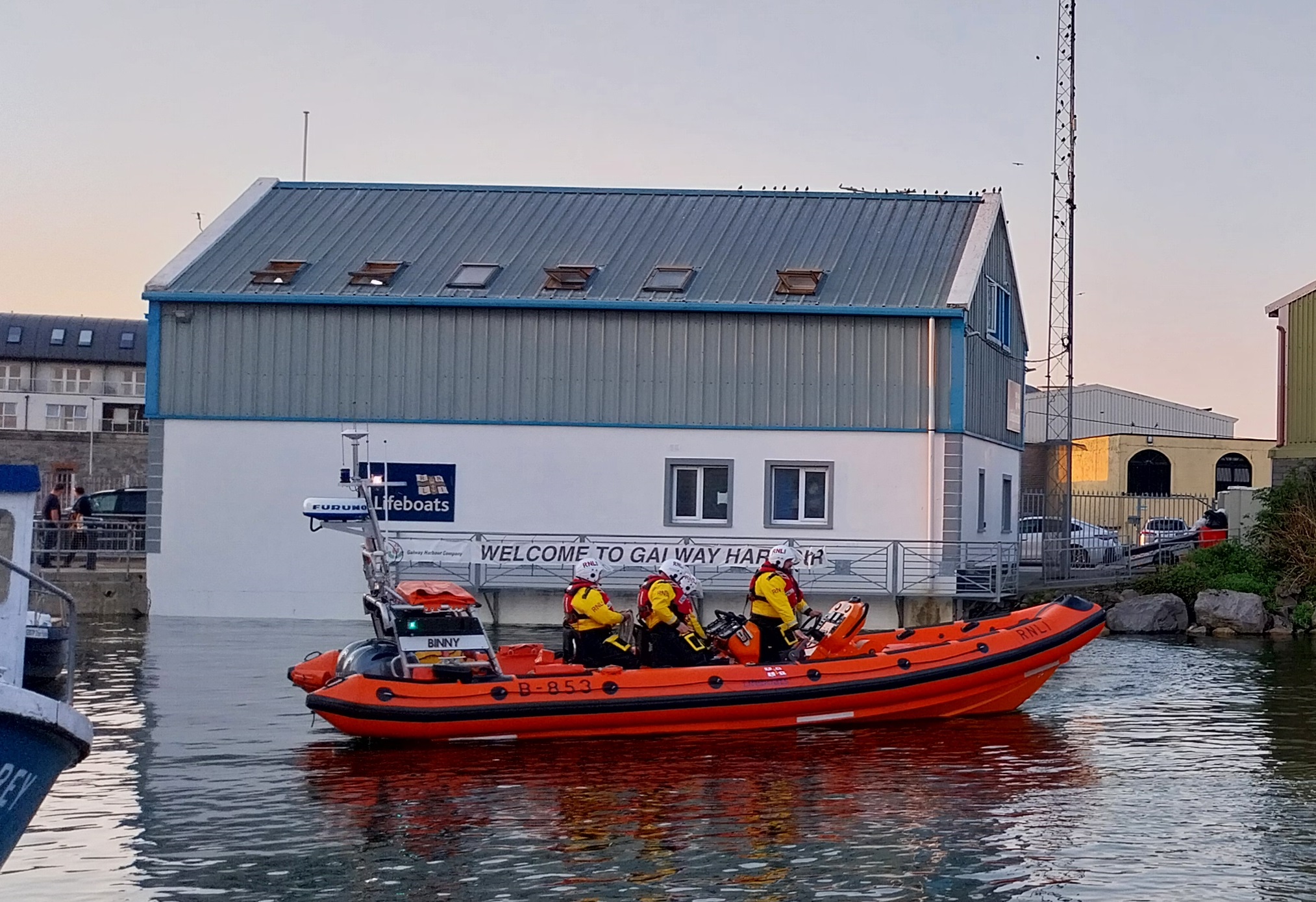Four crew on board an Atlantic 85 lifeboat, on the water just after launching, with the Galway lifeboat station in the background.