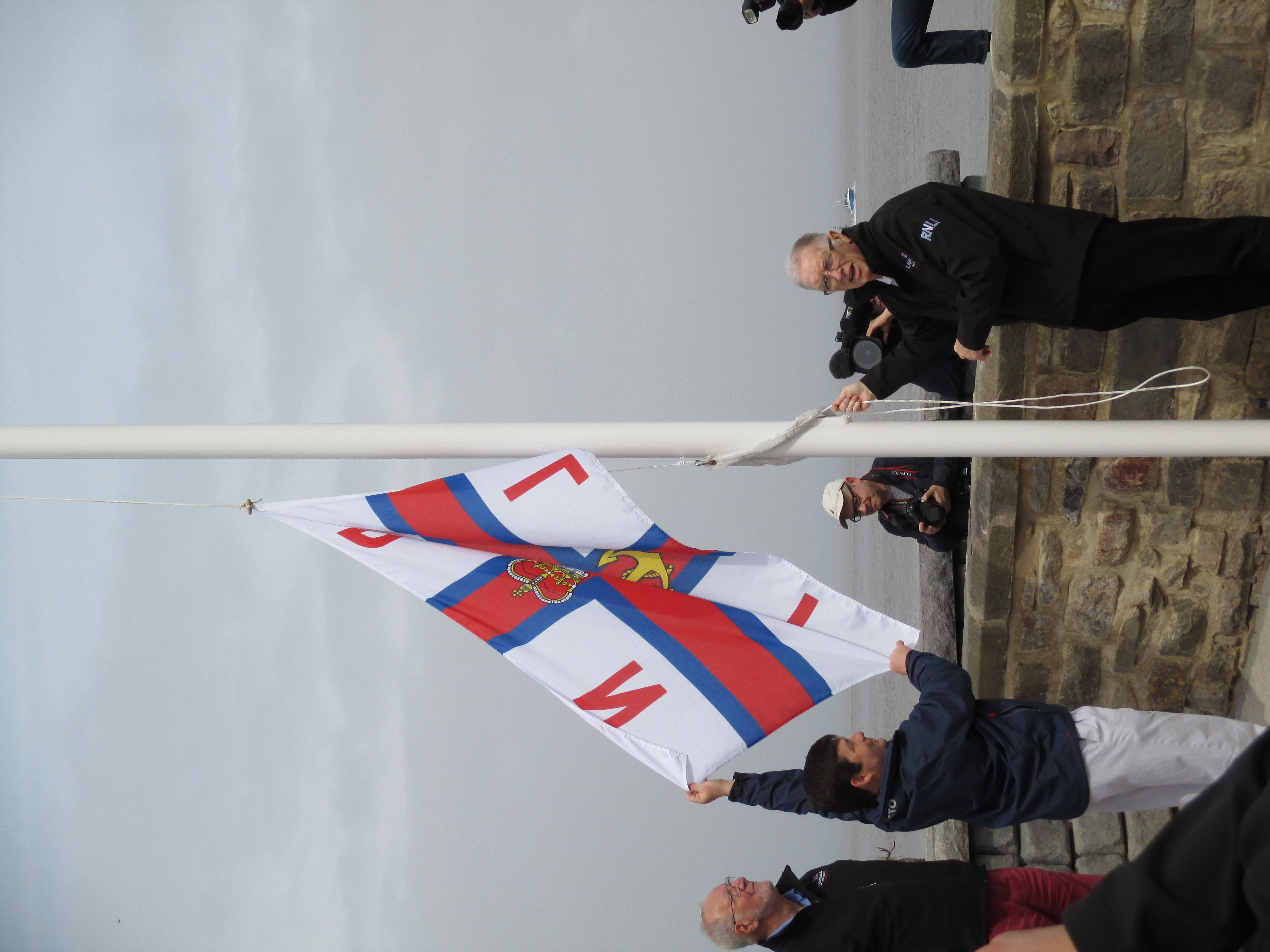 RNLI flag being hoisted for the first time to mark the lifeboat station operational, with Mike Roberts, volunteer RNLI Portishead President, Nigel Jones who was the Area Lifesaving Manager for the region, and Bob Crane volunteer Lifeboat Operations Manager at the time.