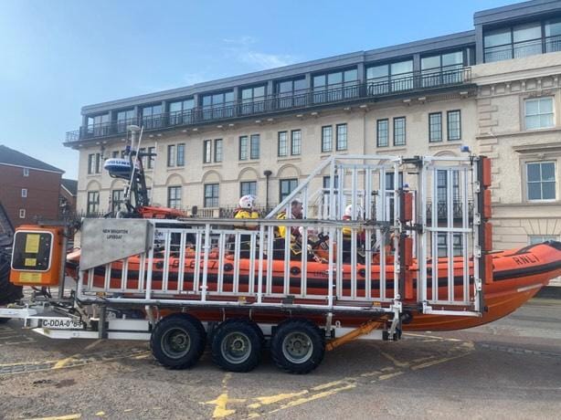 Full frame shot of the lifeboat, from the starboard side, sat in the carriage. Crew can be seen onboard, preparing the boat for service.