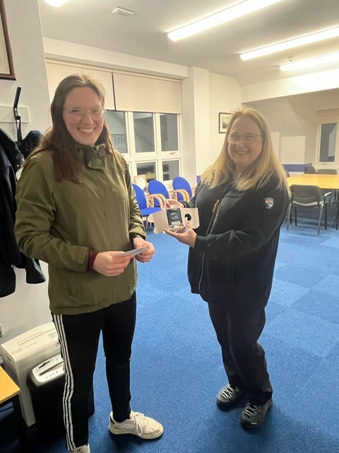Two women, one handing over a pager to the other inside a lifeboat station