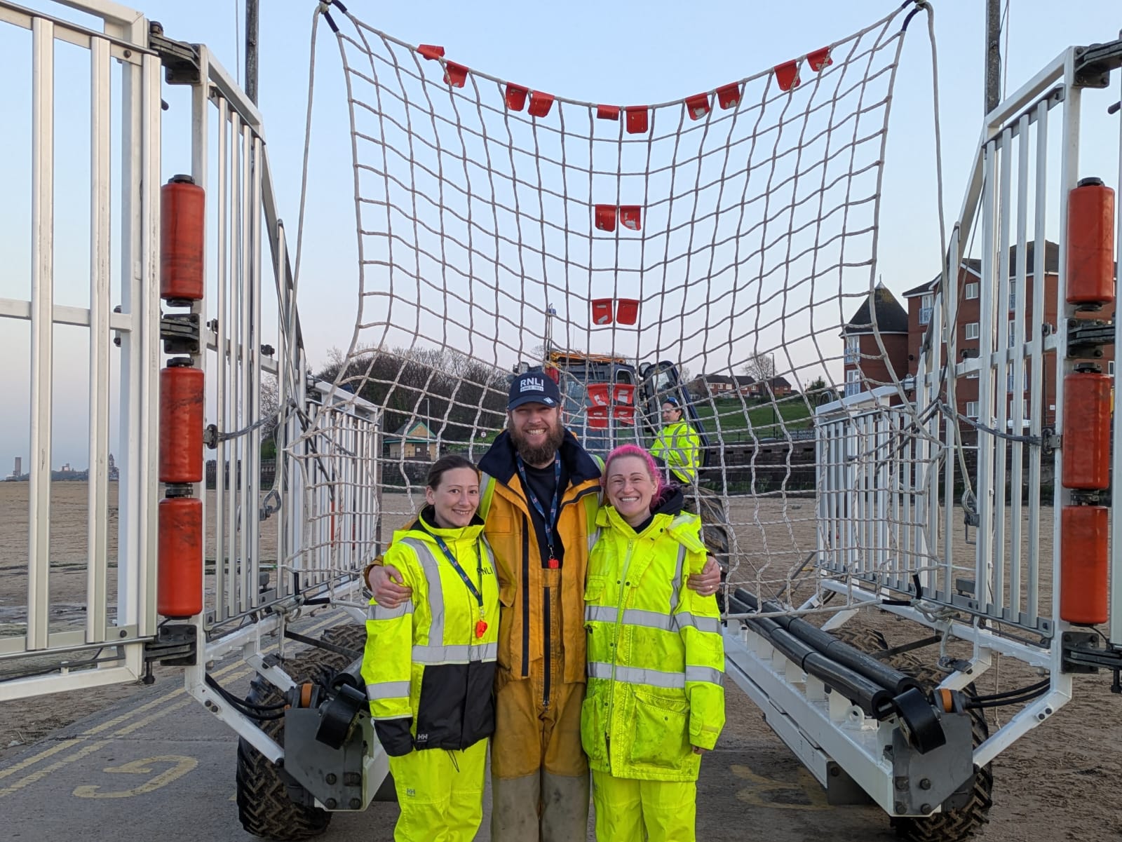 Faye, Lisa and Ben pose, smiling, in front of a recovery net fully rigged inside the recovery carriage for the RNLI.
