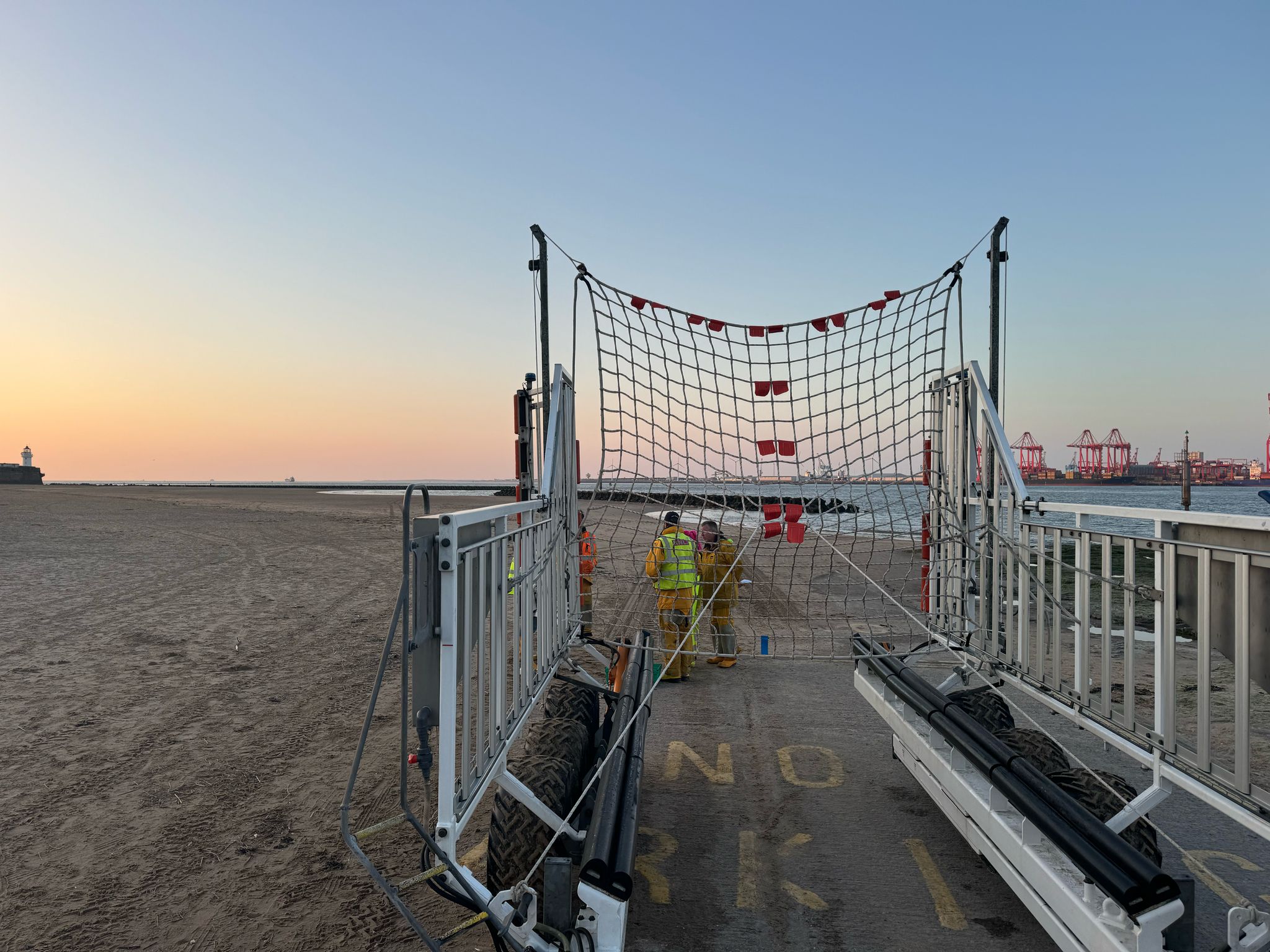 Sunset on New Brighton beach, with orange, pink and golden sky in the background. In the foreground, the recovery carriage can be seen with fully rigged recovery net.
