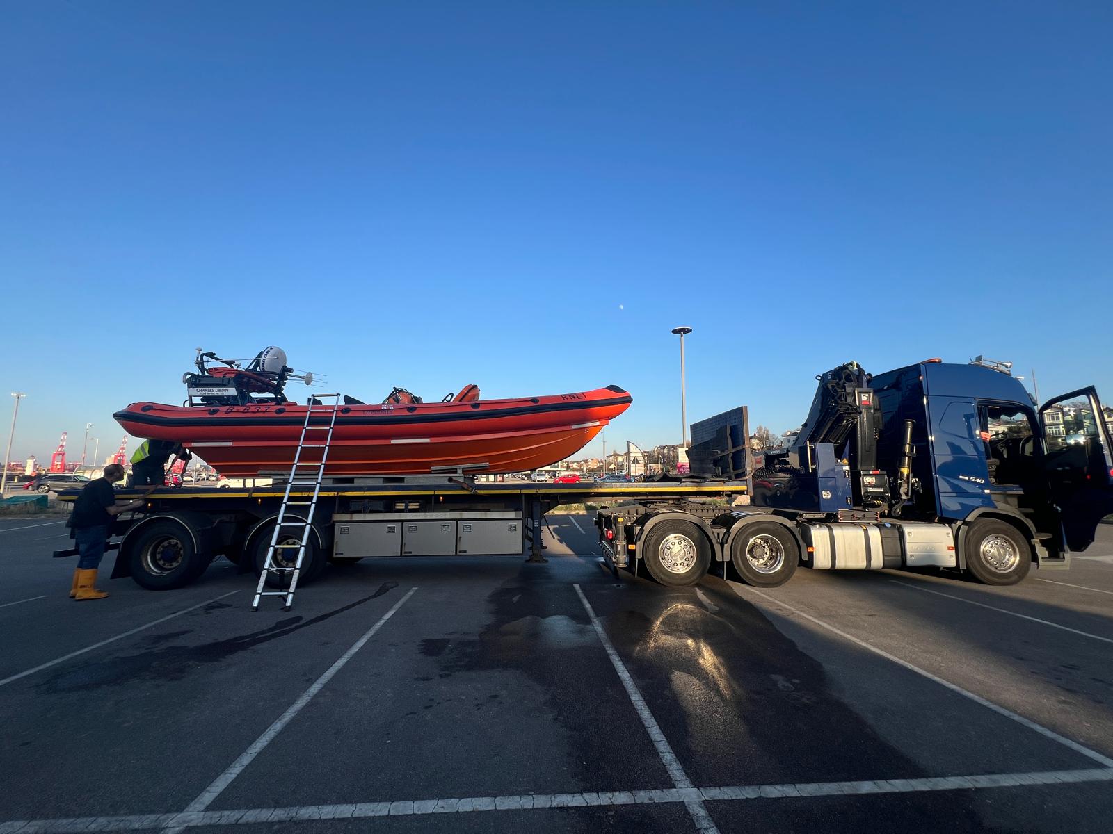 New Brighton RNLI's volunteer crew work, with the help of a ladder, to remove all necessary equipment from the lifeboat. Full side on view of the relief craft on the back of the road transport.