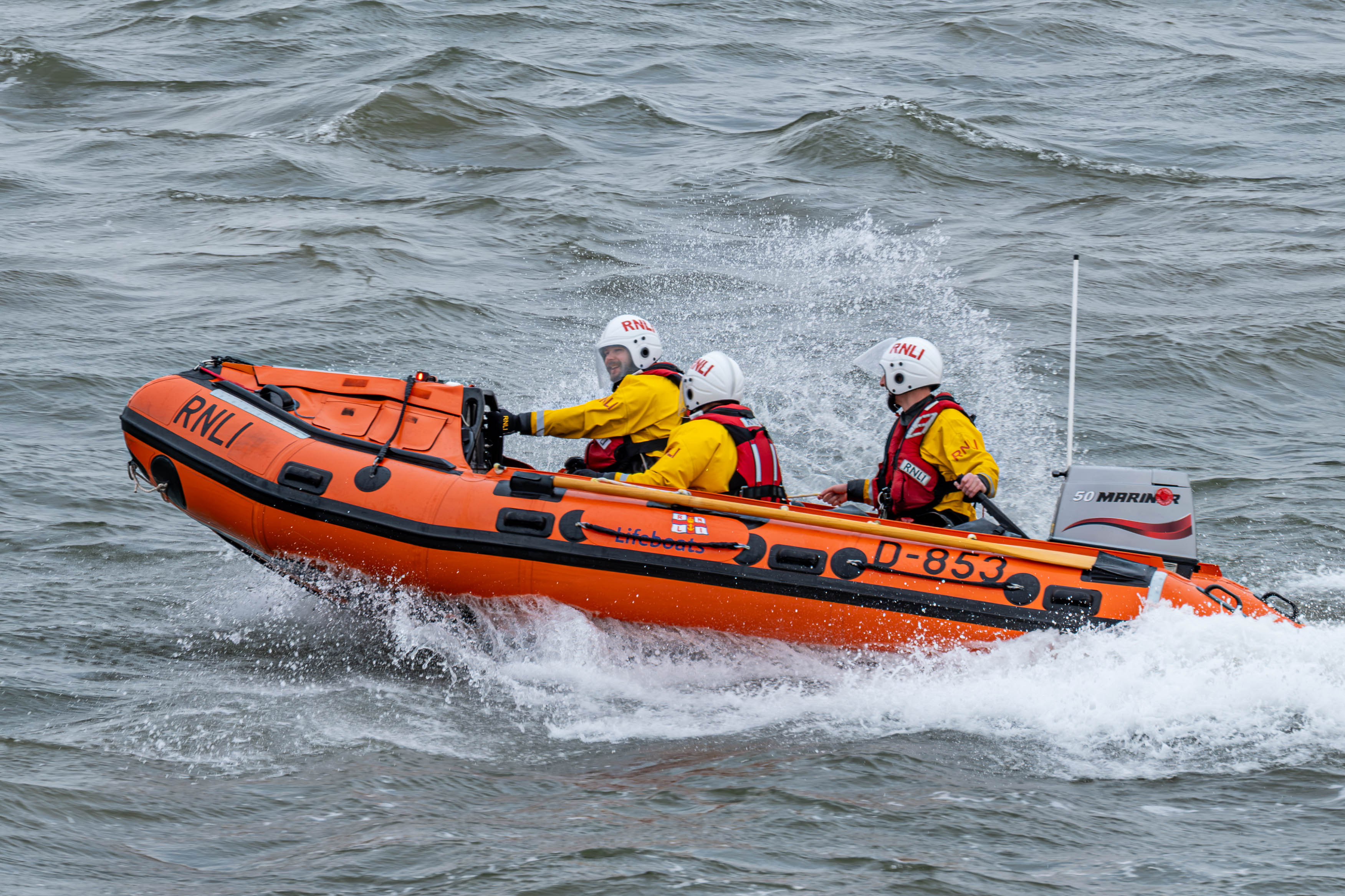D Class inshore lifeboat with three crew aboard travelling right to left with bow wave and spray to rear